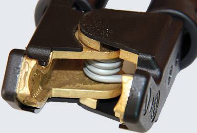 Detailní záběr černě a zlatě lakované bateriové svorky s pružinovým mechanismem.
