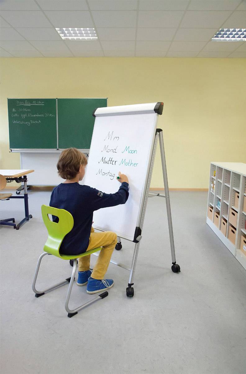 Chlapec sedí na židli ve třídě a na flipchart zapisuje slova začínající na písmeno 'M'.