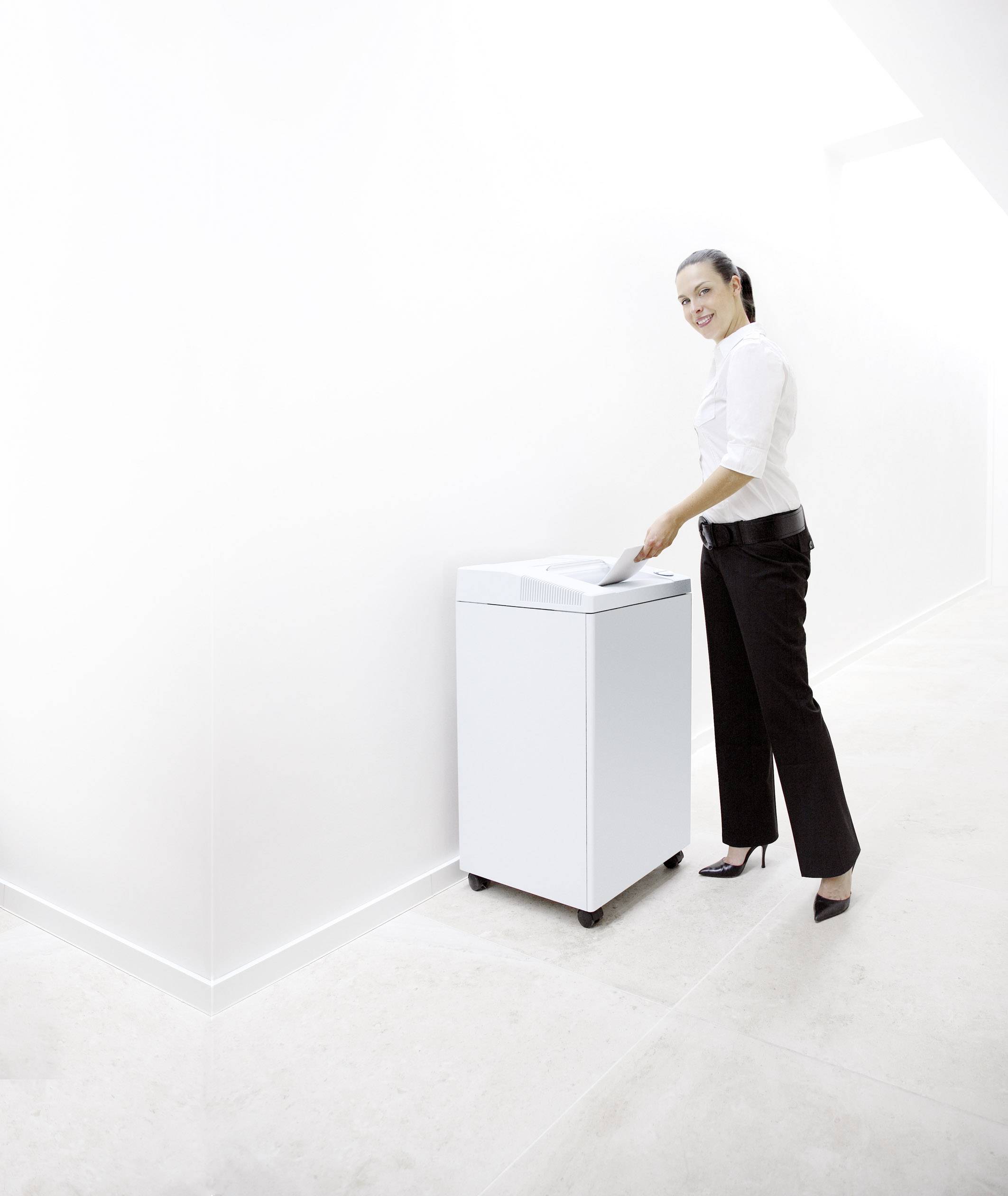 Žena vhazuje papír do bílého odpadkového koše na kolečkách v světlém, minimalistickém prostoru.
