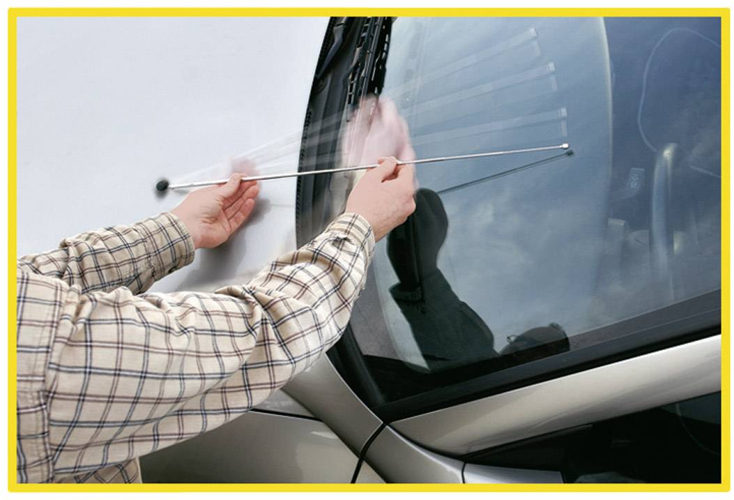 Člověk čistí přední sklo automobilu dlouhou tyčovitou pomůckou.