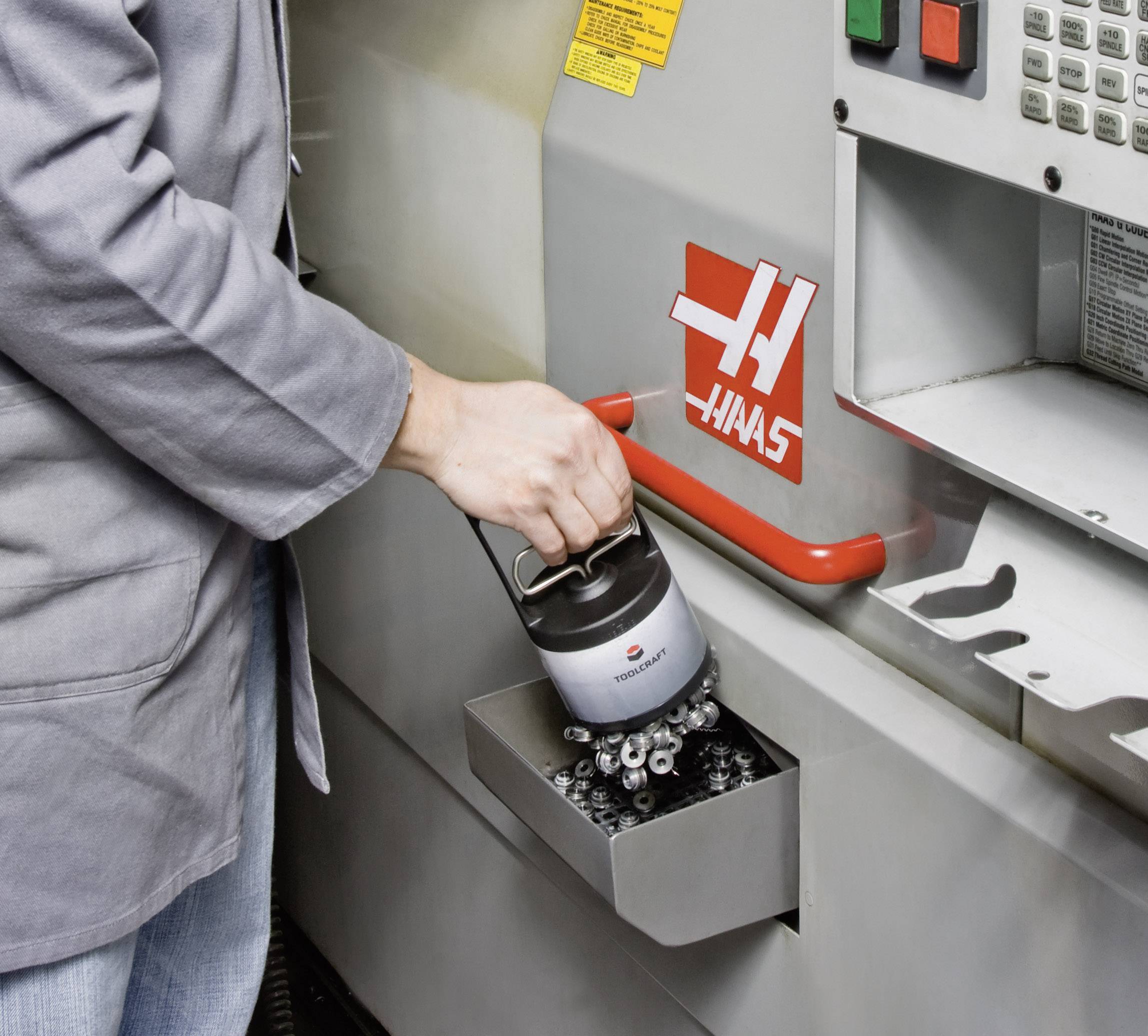 Pracovník vyprazdňuje nádobu s kovovými třískami z CNC stroje. Stroj zobrazuje logo známého výrobce.
