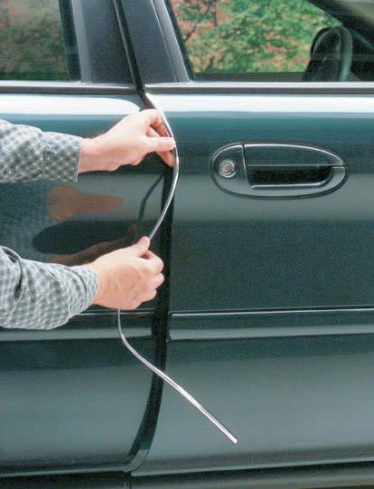 Osoba používá tenkou kovovou tyč k otevření dveří automobilu. Pozornost je zaměřena na techniku odemykání.