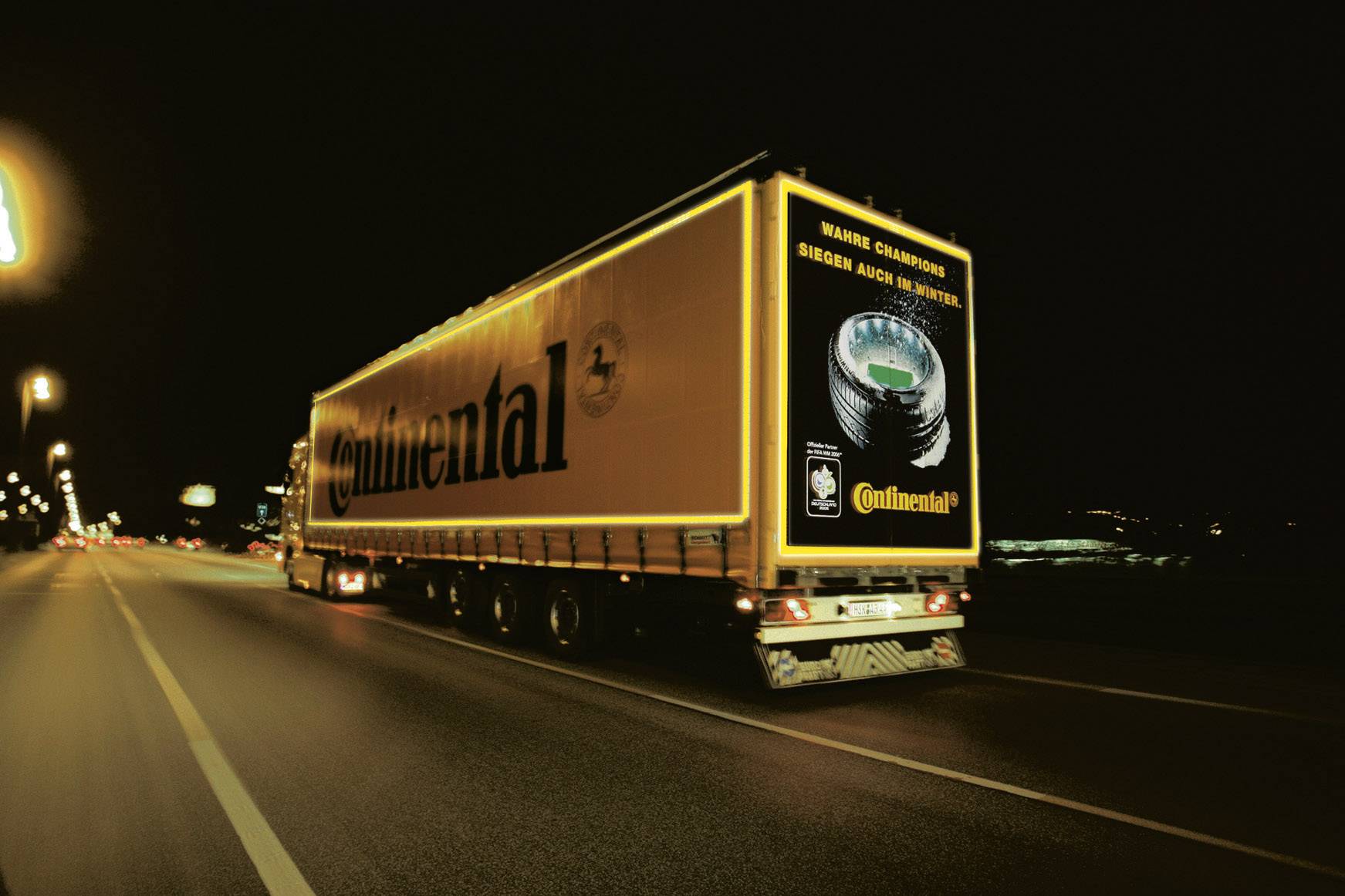 Nákladní automobil s reklamou "Continental" jede v noci po osvětlené dálnici.