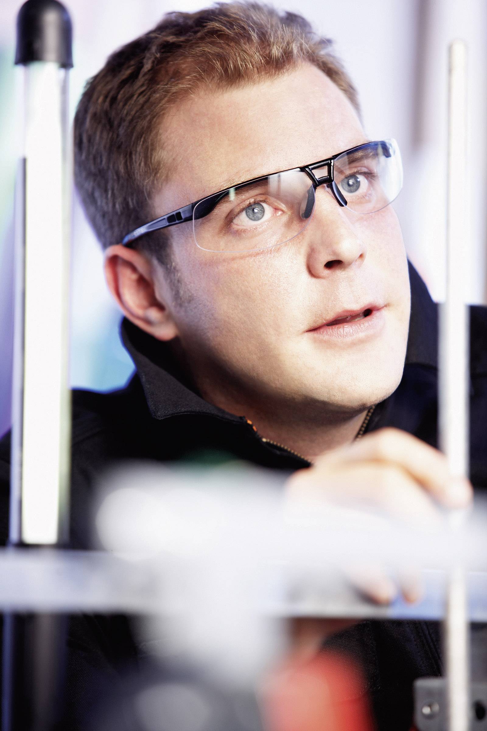 Muž v ochranných brýlích se soustřeďuje na technické práce, pravděpodobně v laboratoři nebo dílně.