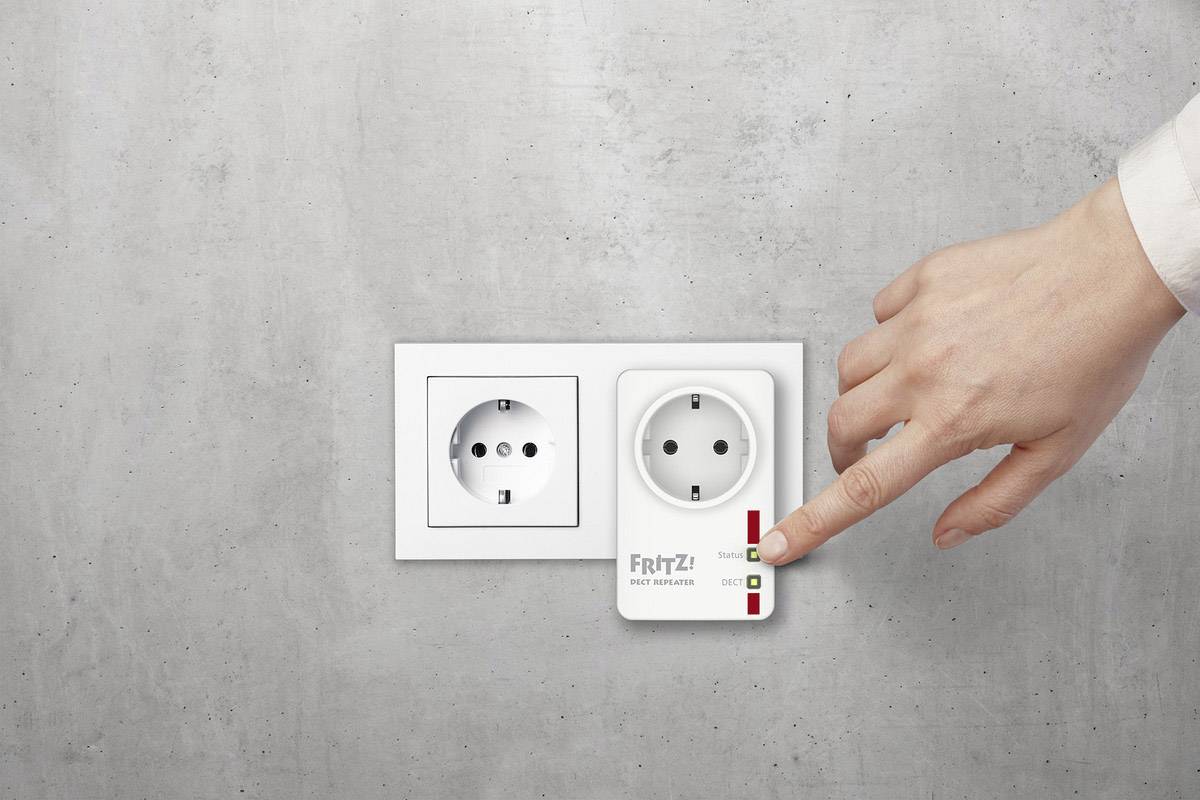 Ruka obsluhuje zásuvkový adaptér 'FRITZ! DECT 200' v nástěnné elektrické zásuvce. Adaptér je zapnutý.