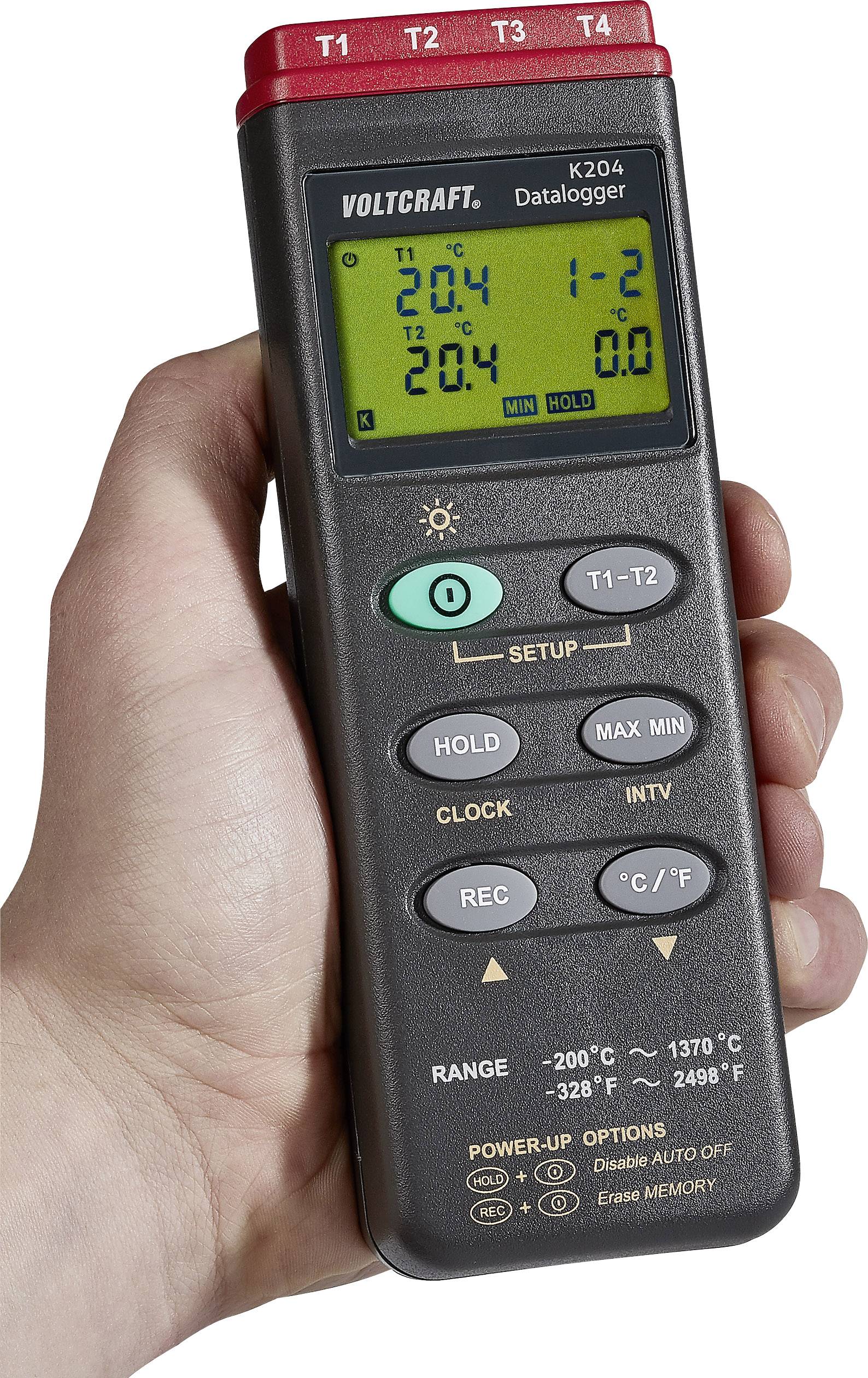 Hånd holder et digitalt termometer med flere knapper og et display, der viser temperaturværdier. Enhed fra Voltcraft, model K204.