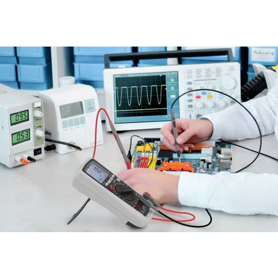 En person tester et elektronisk kredsløb med et multimeter og et oscilloskop for at kontrollere spændings- og signalværdier.