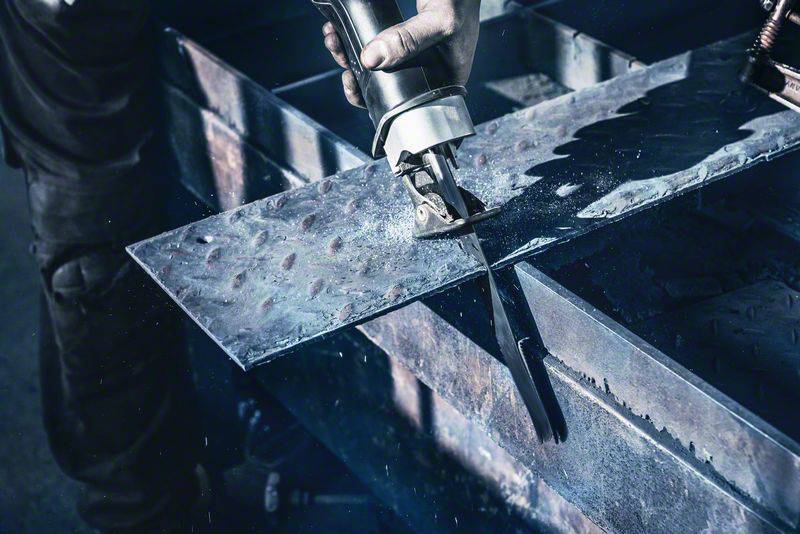 En person skærer i en metalplade med et elværktøj, hvor gnister sprøjter. Vedkommende arbejder på et bygge- eller reparationsprojekt.
