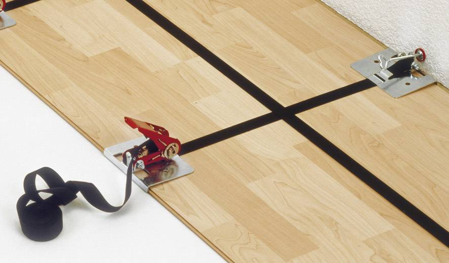 Et trægulv forbindes med spænderemme og metalhjørner for at sikre en stabil forbindelse mellem de enkelte paneler.