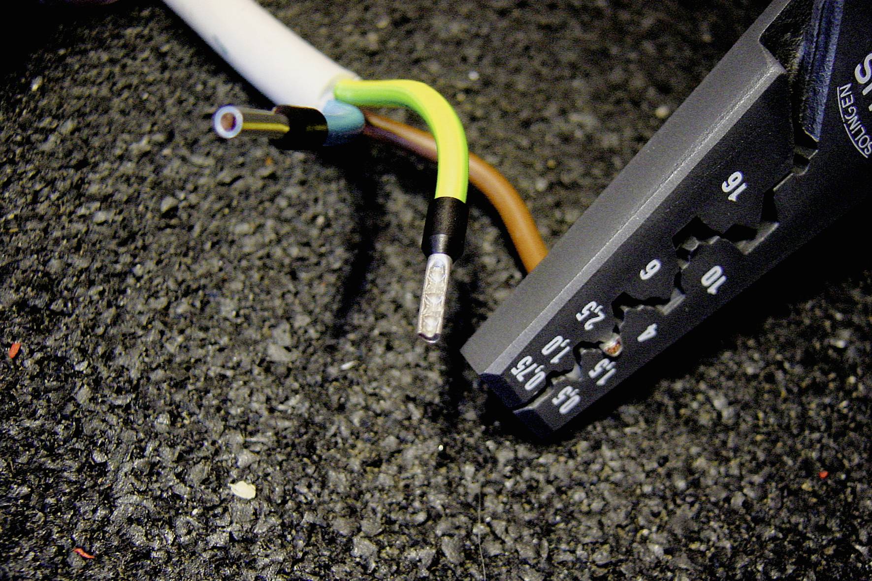 En kabelafisoleringstang er placeret ved siden af et kabel med tre synlige ledere på en mørk baggrund.