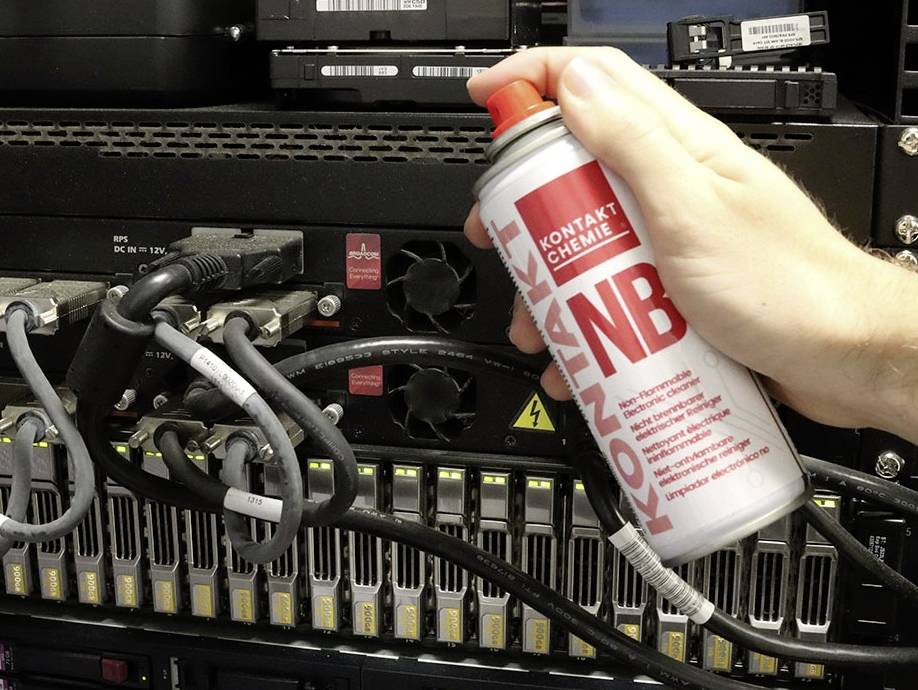 En hånd sprayer trykluft på et serverrack med kabler og blinkende lys for at fjerne støv.