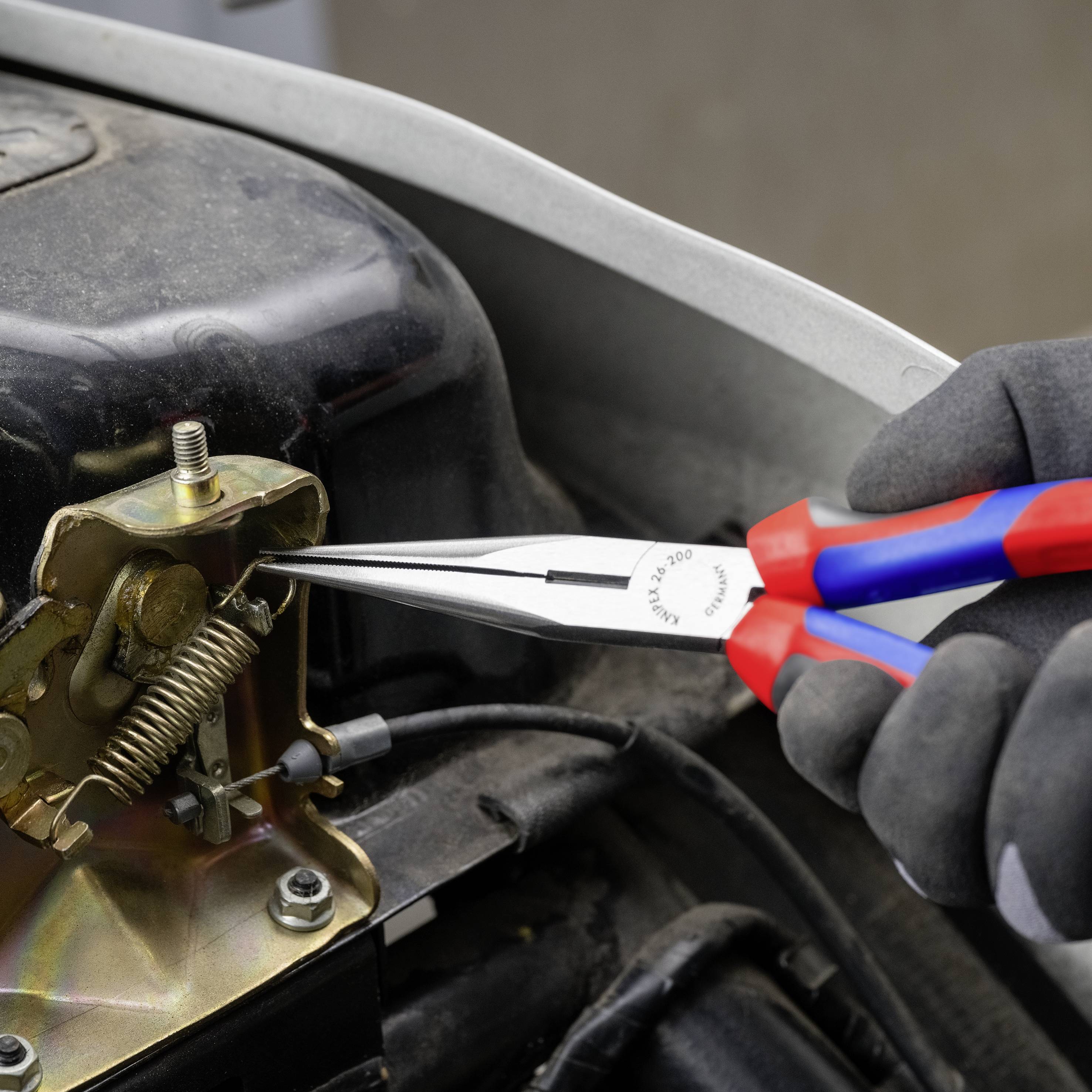 En person bruger en tang til at arbejde på en mekanisme i et køretøjs motorrum. Fokus er på præcis reparation.