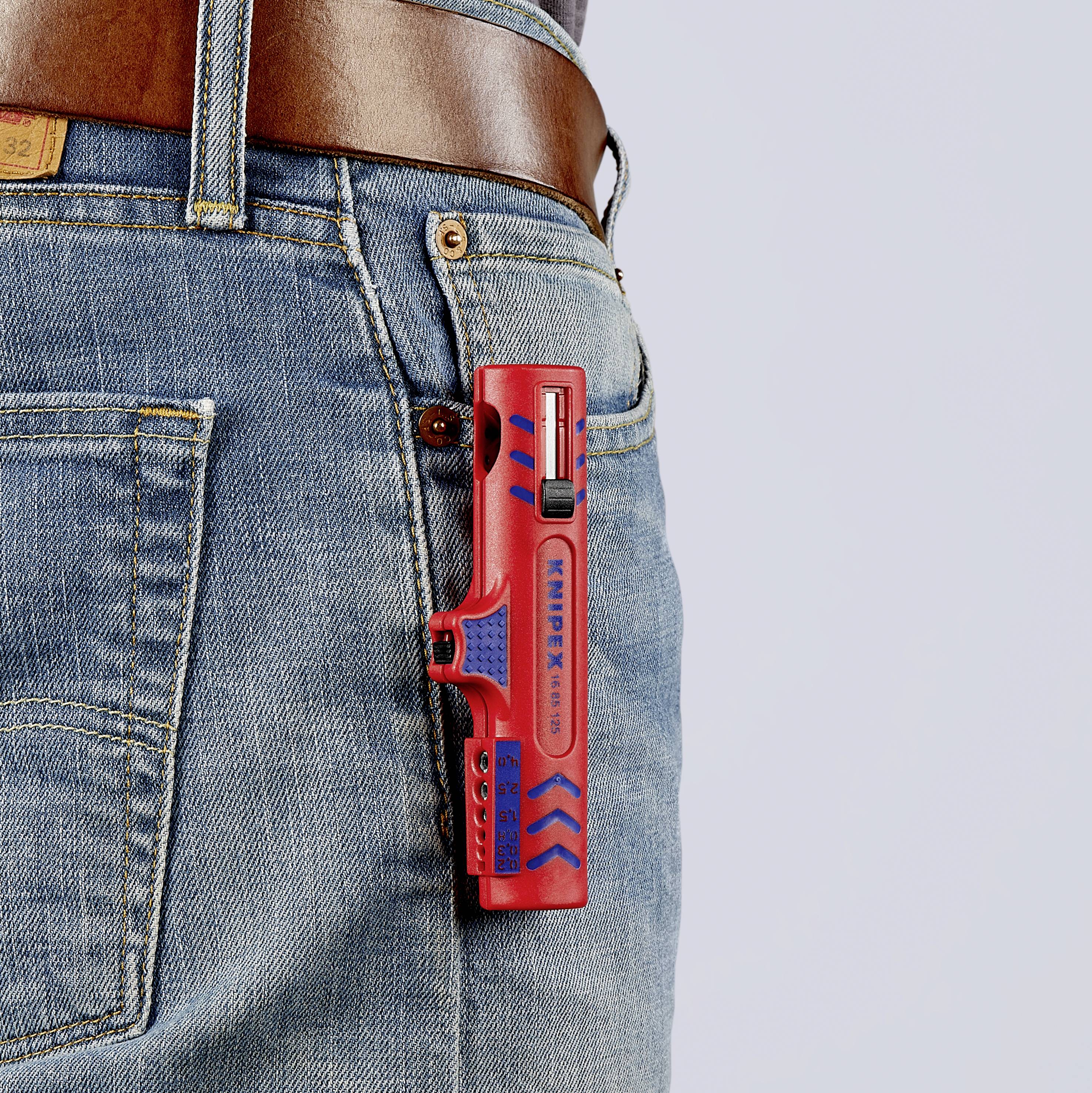 Et rødt multiværktøj sidder i baglommen på et par blå jeans, sikret af et brunt lærbælte.