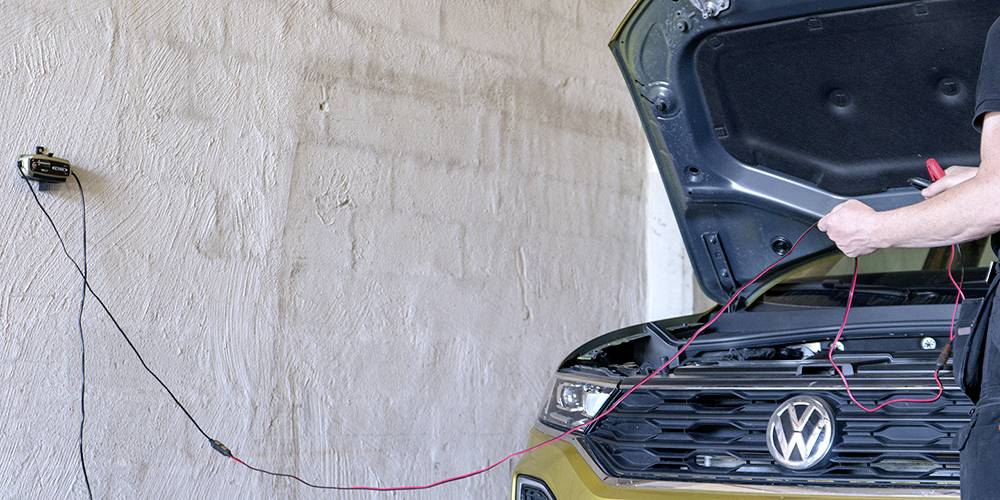 En person lader bilen ved hjælp af en oplader på væggen. Motorhjelmen er åben, og bilen holder i en garage.