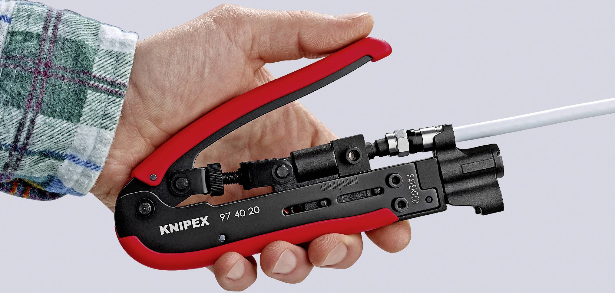 En hånd holder en rød crimptang fra mærket Knipex, som bearbejder et kabel.