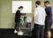 En person viser noget i en kasse til to andre personer i et fitnesscenter. Et whiteboard hænger på væggen i baggrunden.