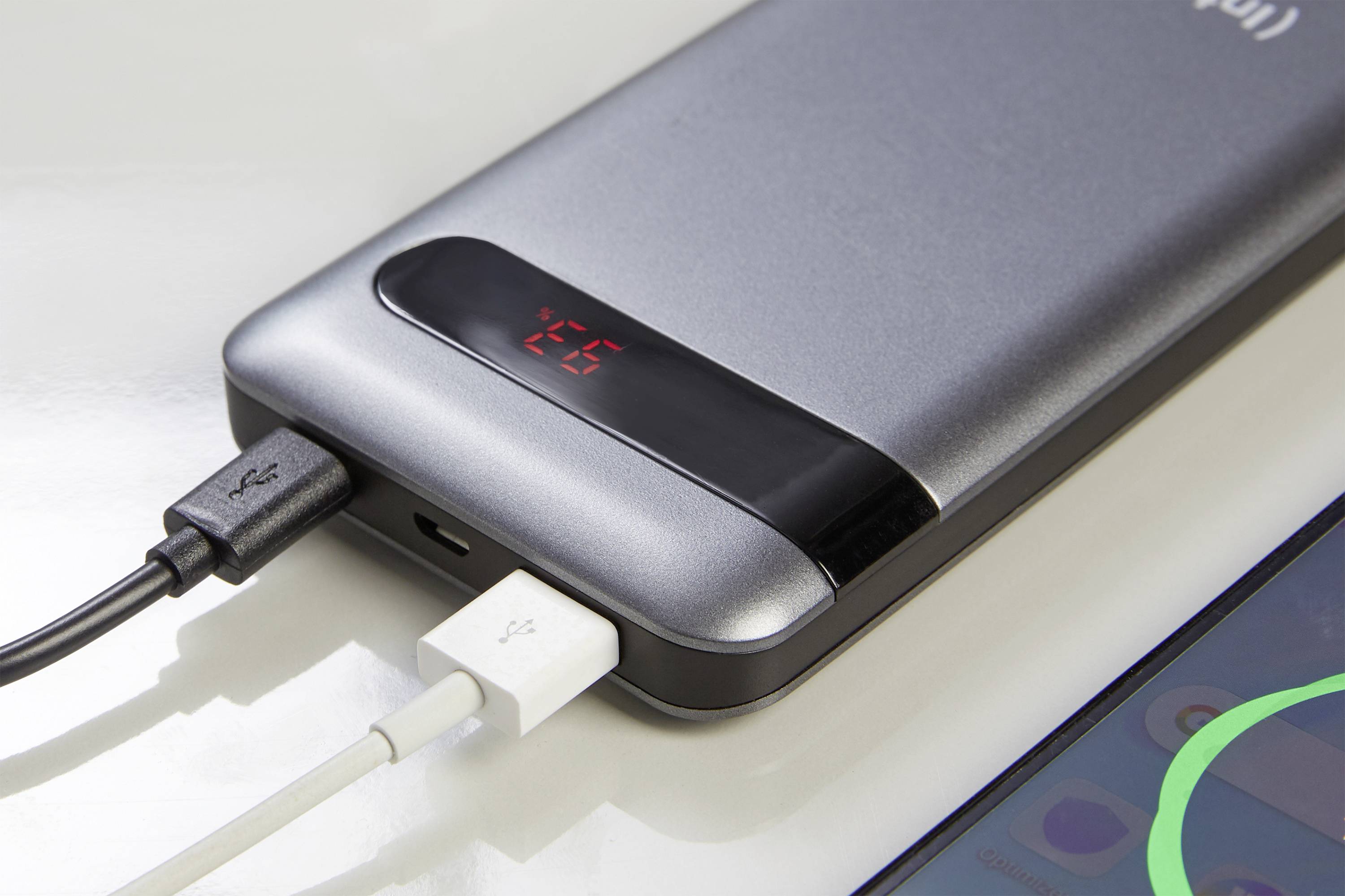 Et sølvfarvet powerbank viser tallet 25 på et digitalt display og oplader en enhed via to tilsluttede kabler.