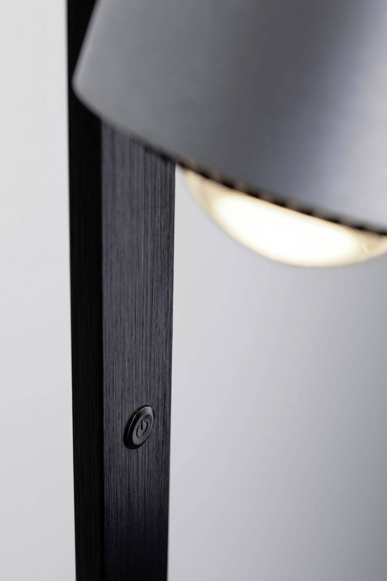 Sort gulvlampe med rund, drejelig lampeskærm i metal og synlig lyskilde, med integreret kontakt ved lampens base.