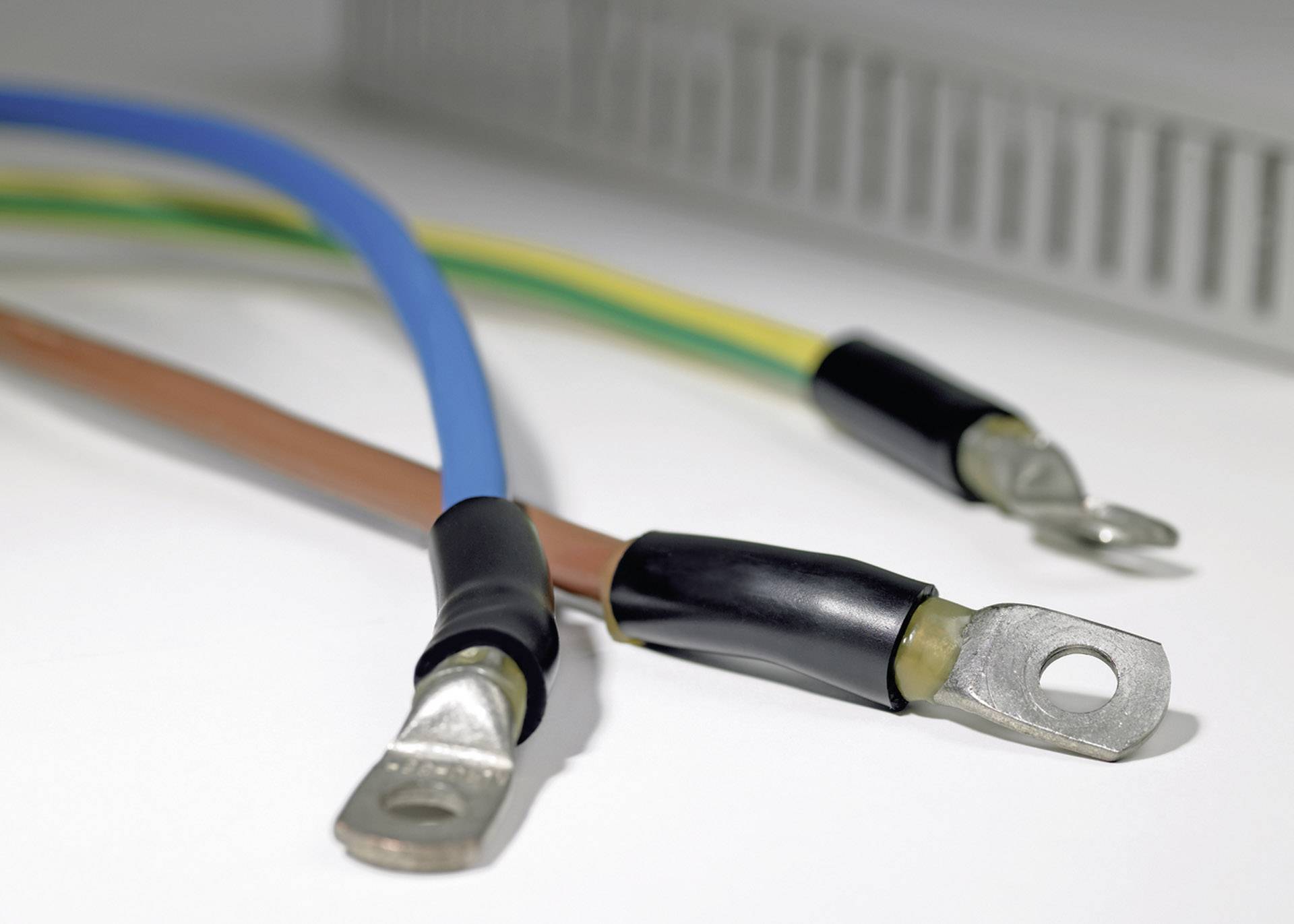 Tre elektriske kabler med metalender, isoleret i blå, brun og gul-grøn, ligger ved siden af hinanden på en hvid overflade.