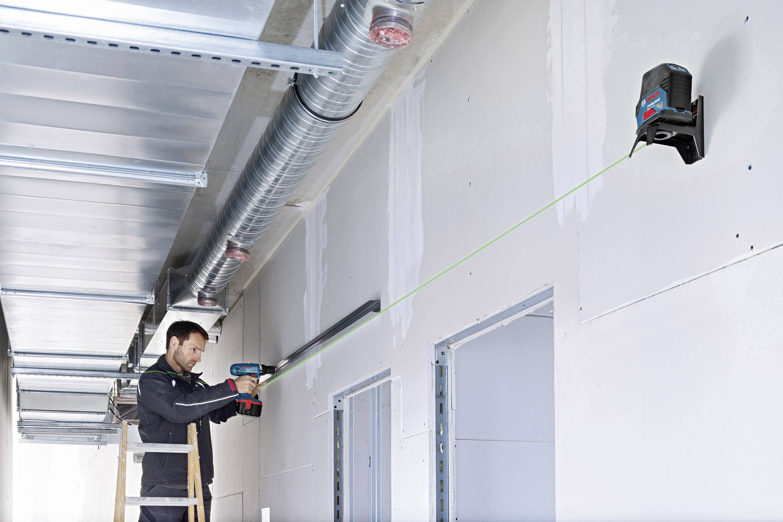 En person arbejder på en væginstallation med et værktøj, der projicerer en grøn laserlinje for at sikre præcis justering.