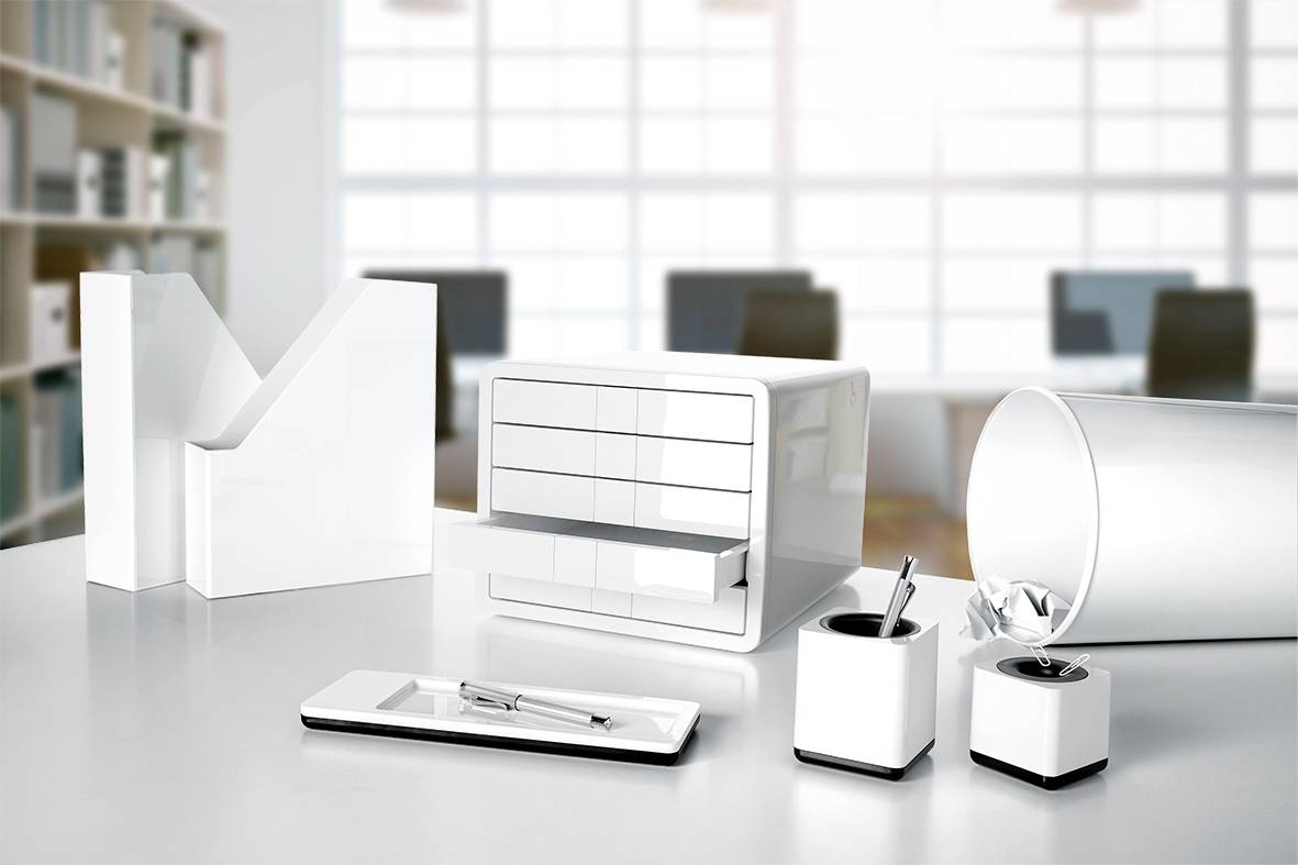 Et moderne skrivebord i hvid, minimalistisk stil med hvide organisatorer, penneholder og dokumentholder. I baggrunden slørede kontormøbler.