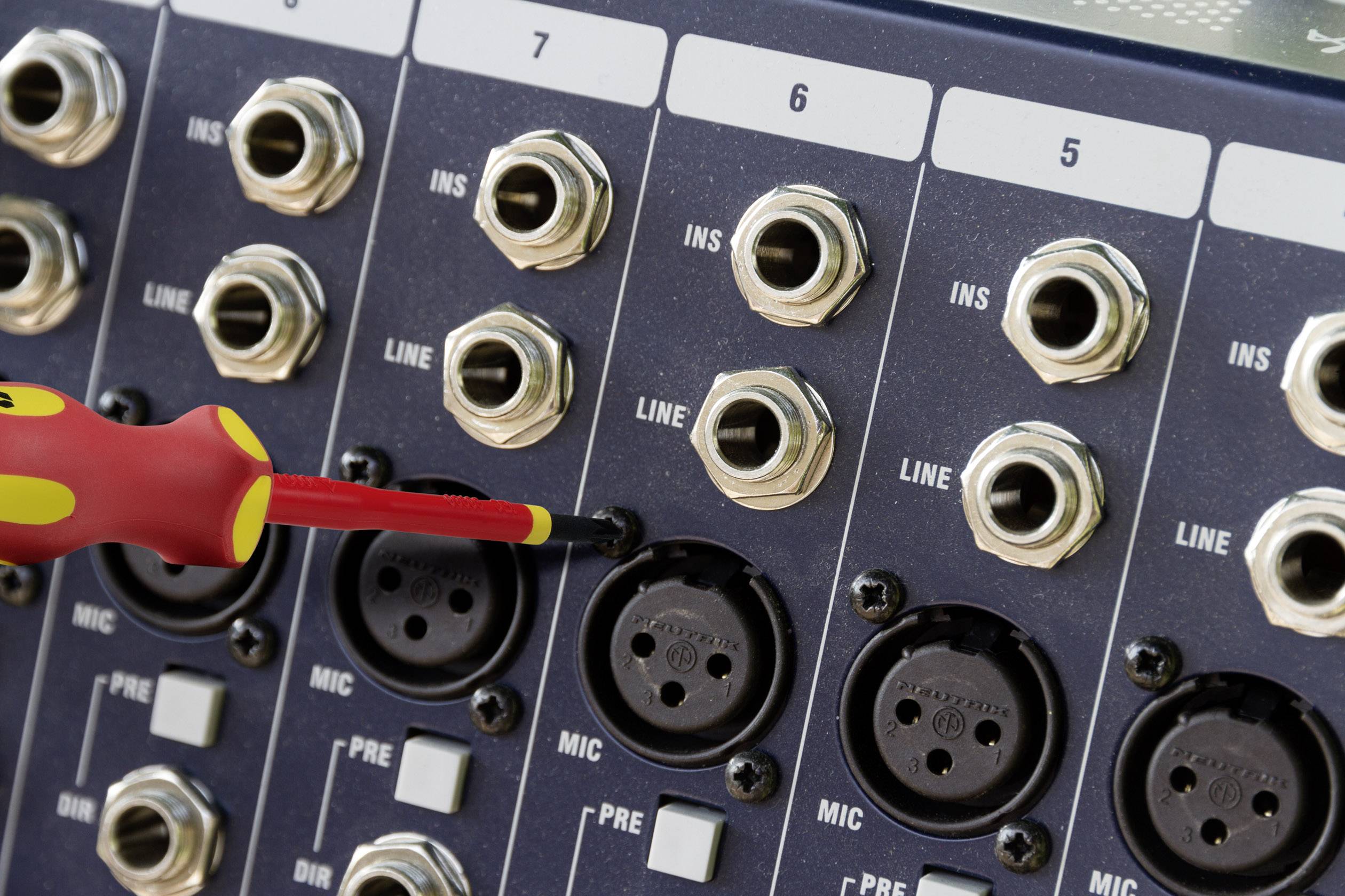 Nærbillede af et mixerbord med XLR- og jackstik-indgange. En skruetrækker justerer en tilslutning i MIC-Pre-rækken.