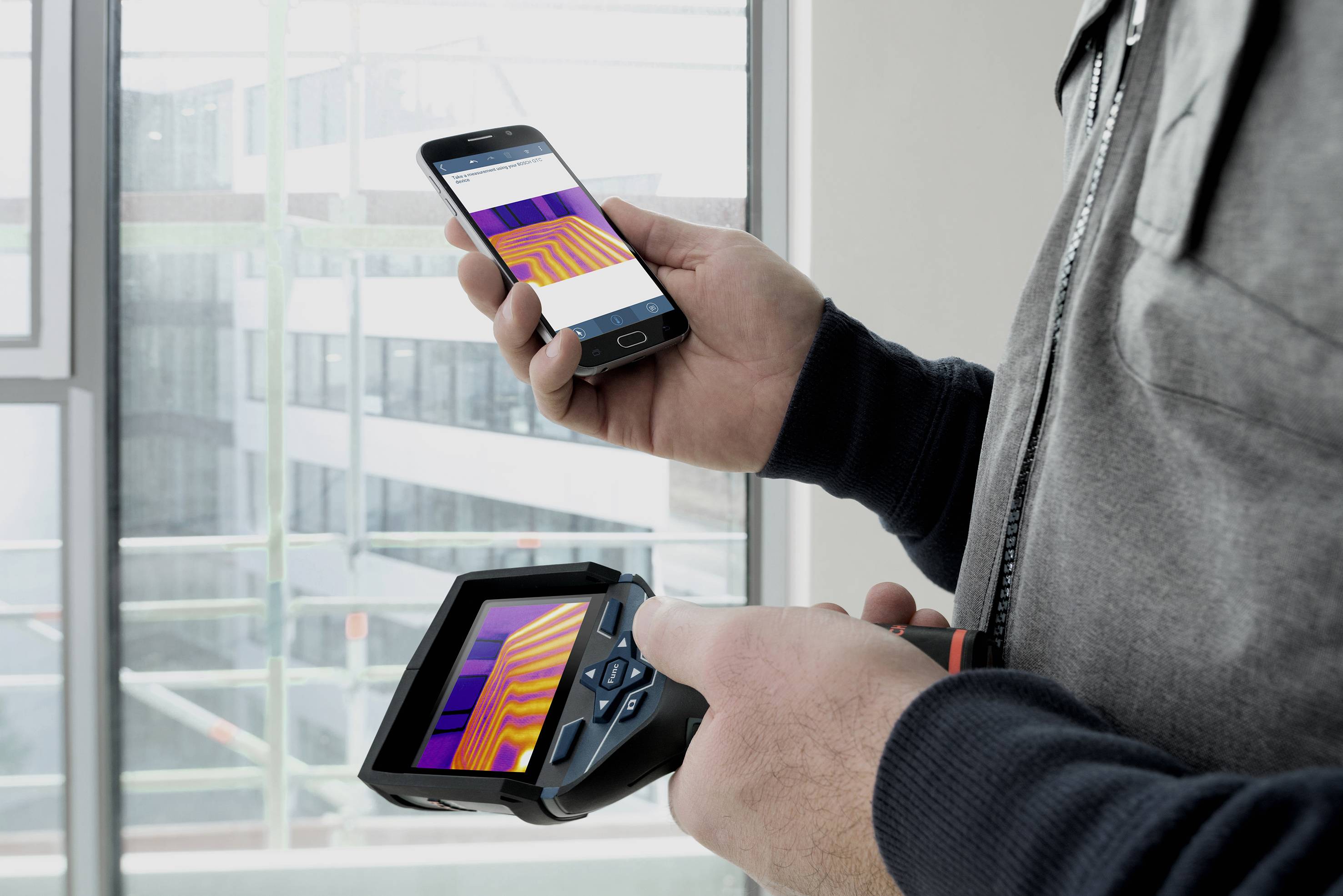 En person holder en mobil enhed til temperaturmåling i hånden. En smartphone viser de samme måledata.