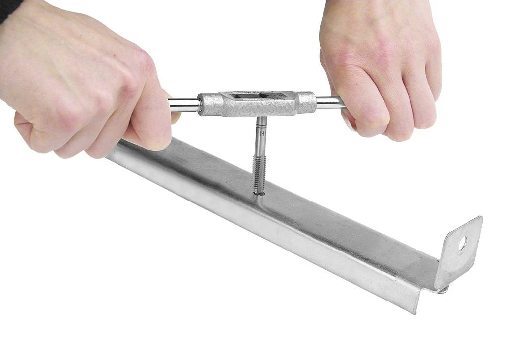 En person bruger en gevindtap til at skære et indvendigt gevind i en metalprofil. Hænderne holder værktøjet, som drejes ind i metallet.