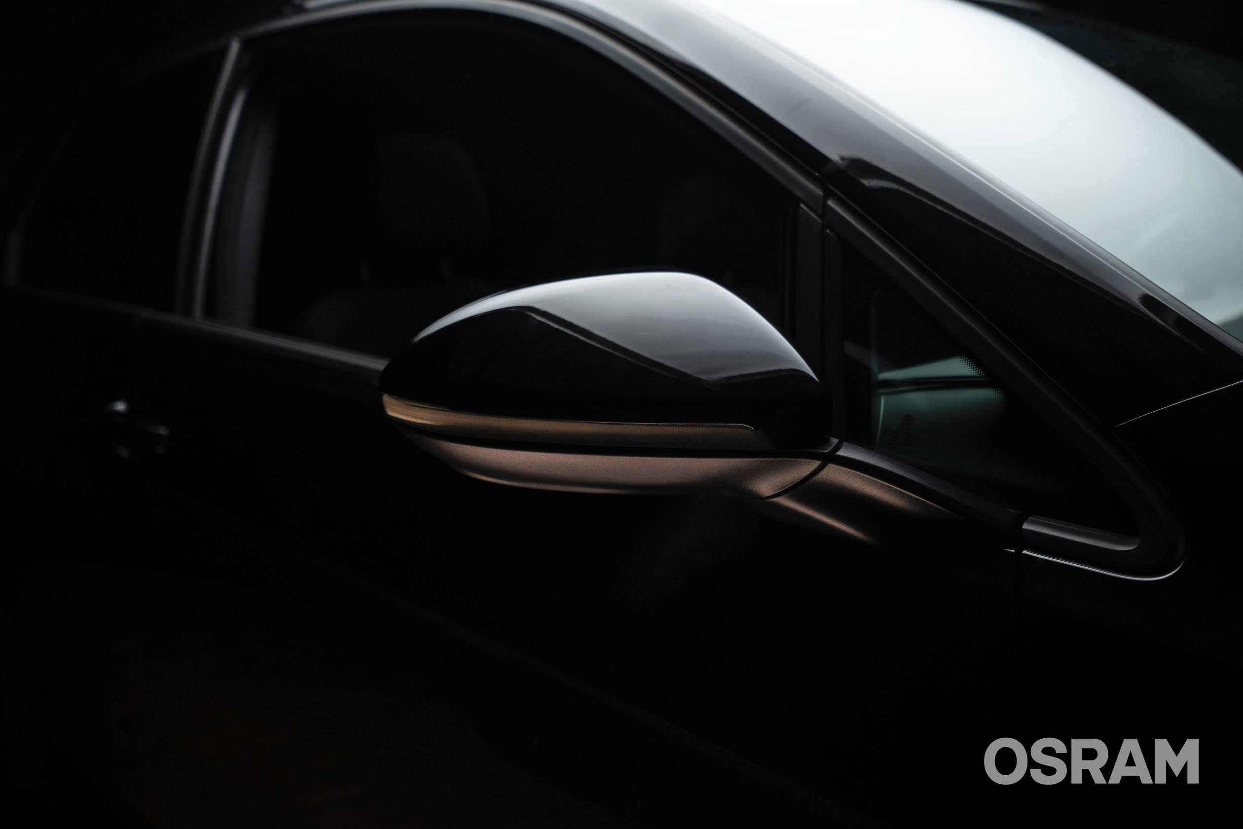 Sidespejl på en sort bil, fokus på blank overflade og elegant form. Mærkelogo 'OSRAM' nederst til højre i billedet.