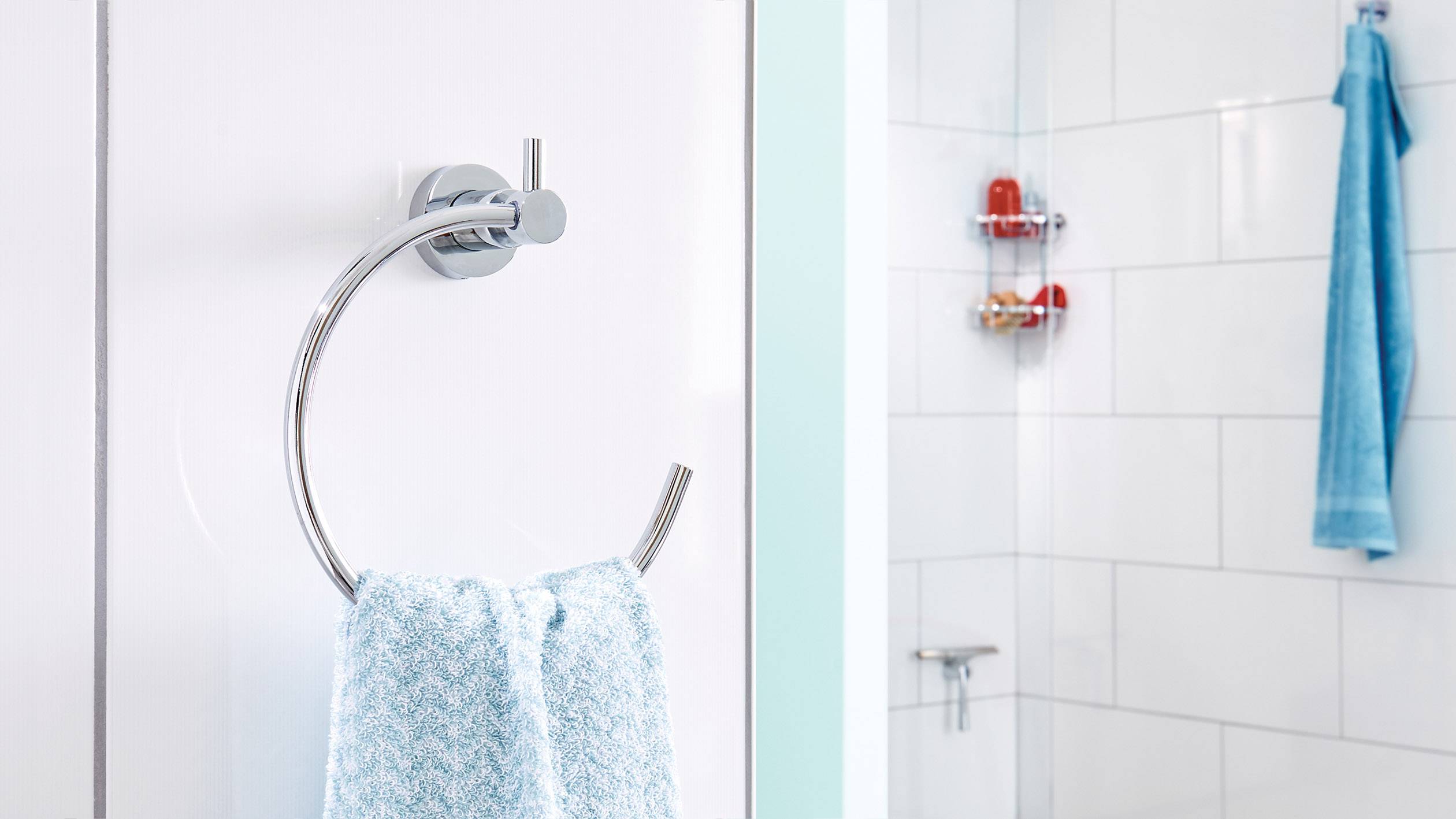 Håndklædeholder på væggen med et blåt håndklæde; i baggrunden en bruseniche med toiletartikler og et blåt håndklæde.