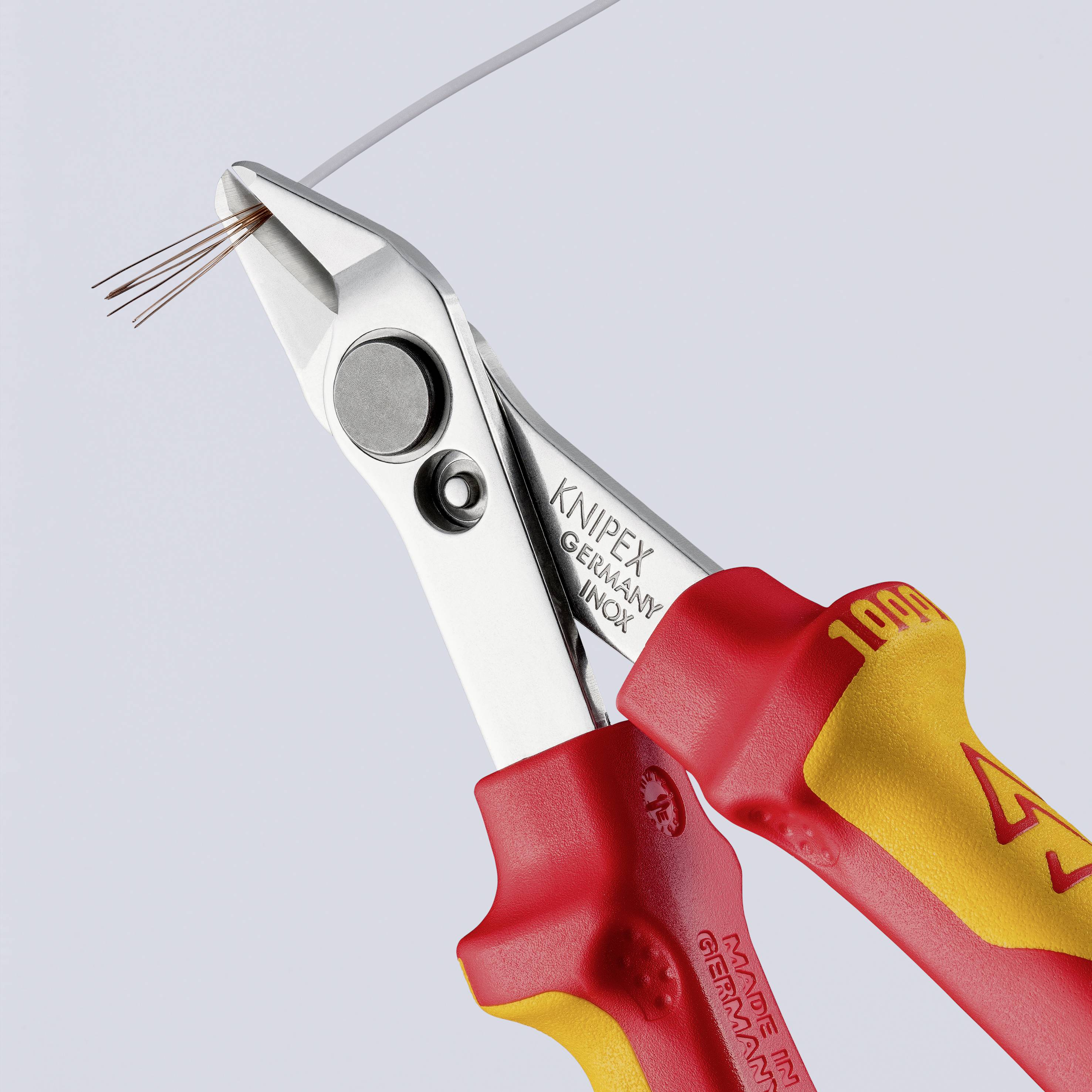 En rød Knipex-tang klipper en sølvfarvet ledning over. Den har ergonomiske håndtag og produceres i Tyskland.