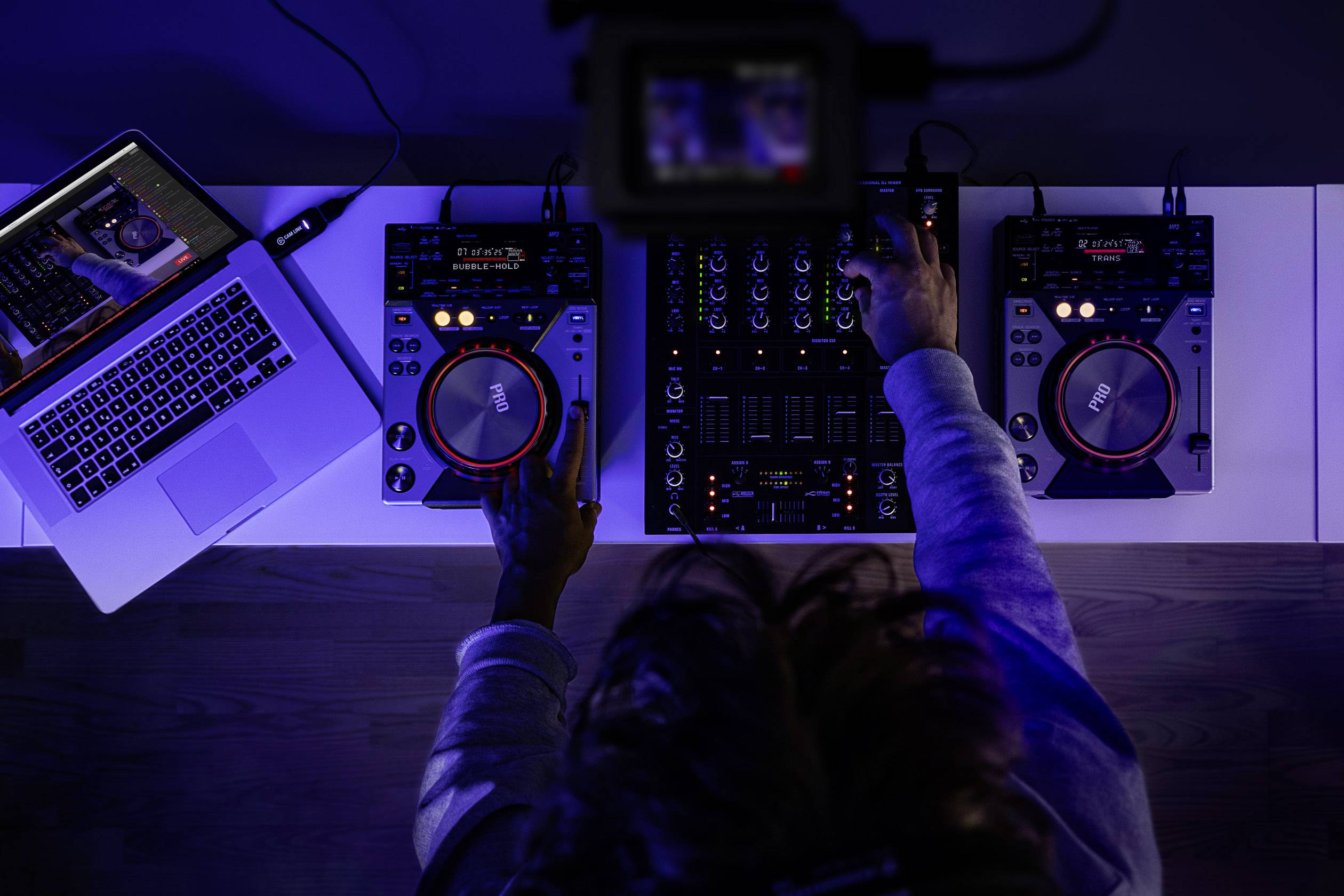 En person blander musik ved hjælp af et mixerbord og to pladespillere, ved siden af en bærbar computer.