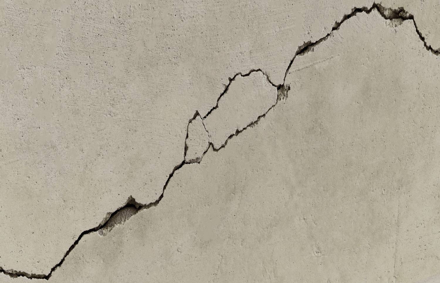 Nærbillede af en revnet betonmur med en lang diagonal revne, der løber fra nedre venstre til øvre højre.