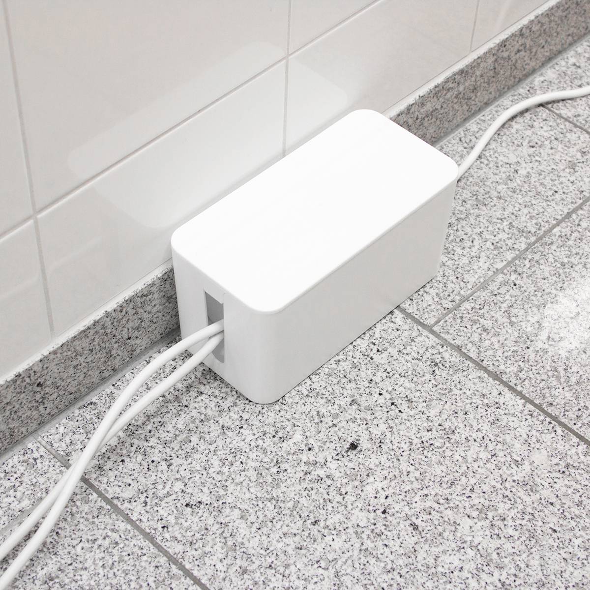 Hvid kabelbox på et gråt flisegulv for at sikre orden. Kabler løber organiseret gennem boksen.