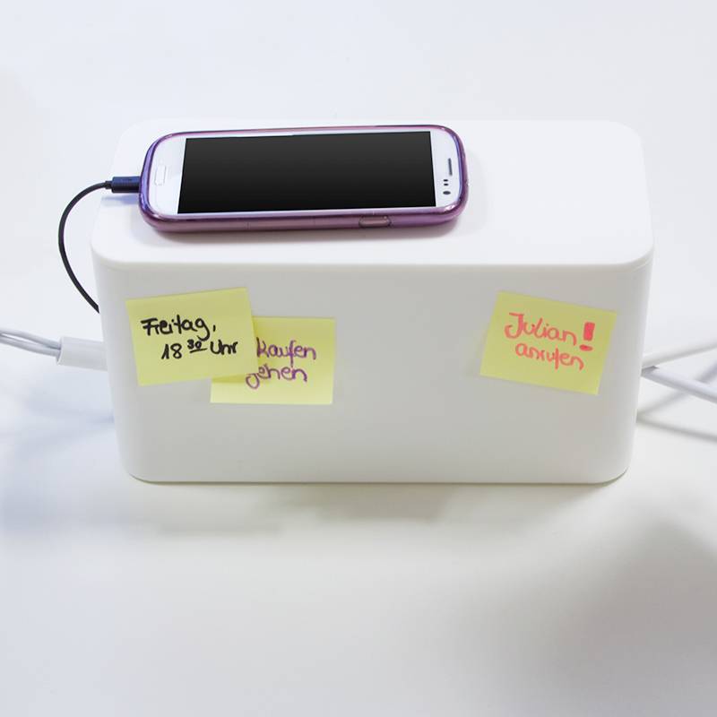 En smartphone oplader på en hvid æske. To sticky notes er påsat: til venstre 'Fredag kl. 18 - gå ud og handle', til højre 'Ring til Julian'.
