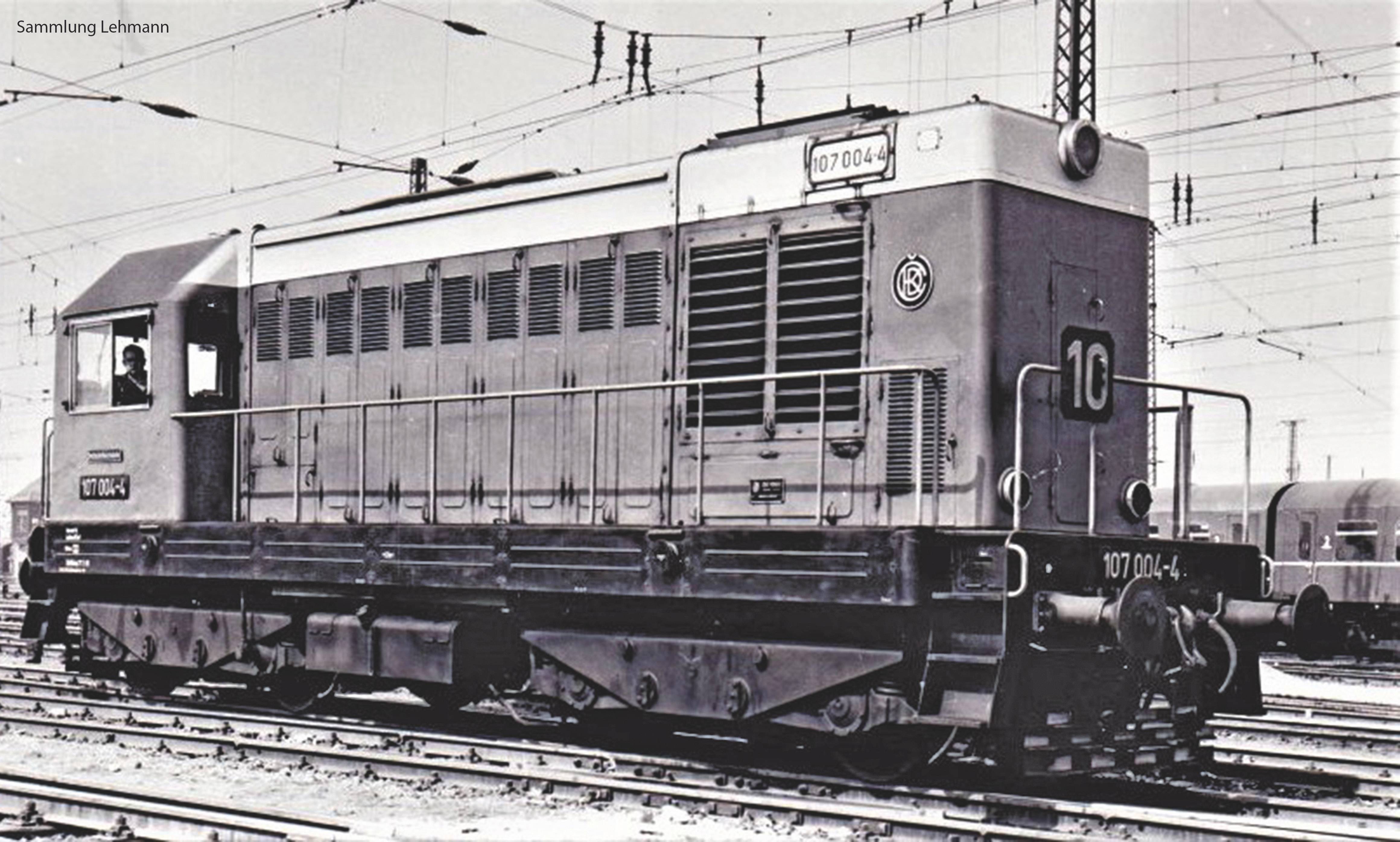Sort-hvid foto af et historisk lokomotiv med påskriften '107 004-4', placeret på skinner. Køreledninger og sporskifter ses i baggrunden.