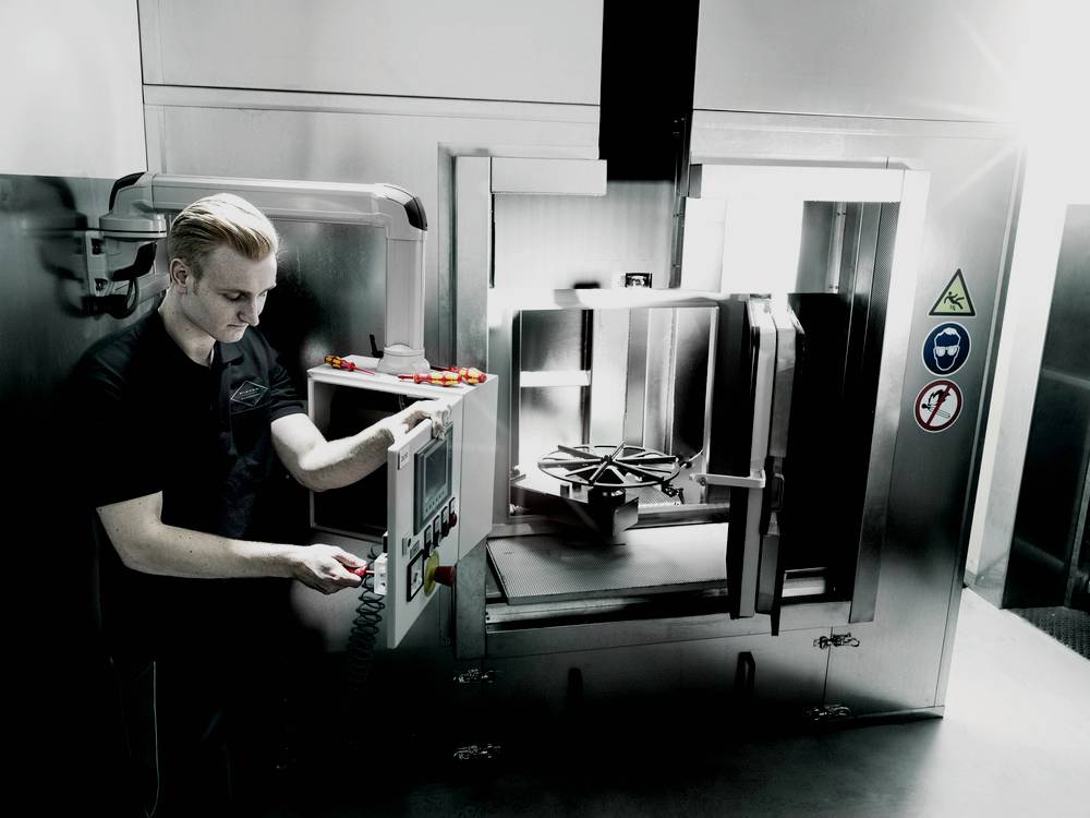 En person betjener en industriel maskine med et betjeningspanel. Advarsels- og sikkerhedssymboler er påsat maskinen.