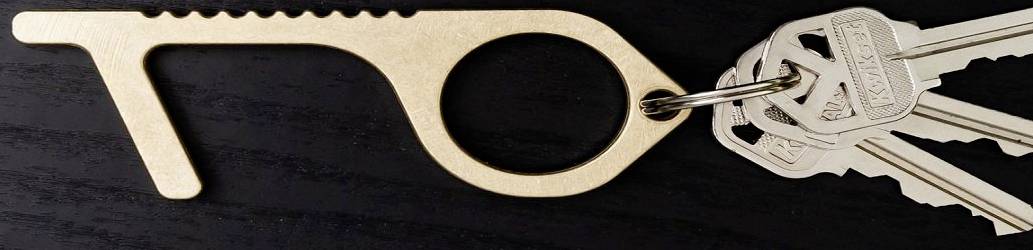 Et berøringsfrit døråbningsværktøj lavet af metal, fastgjort til en nøglering med tre nøgler, på en mørk baggrund.