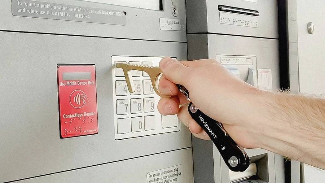 Et menneske bruger et nøgleværktøj til at trykke på pengeautomatens taster for at undgå direkte hudkontakt.