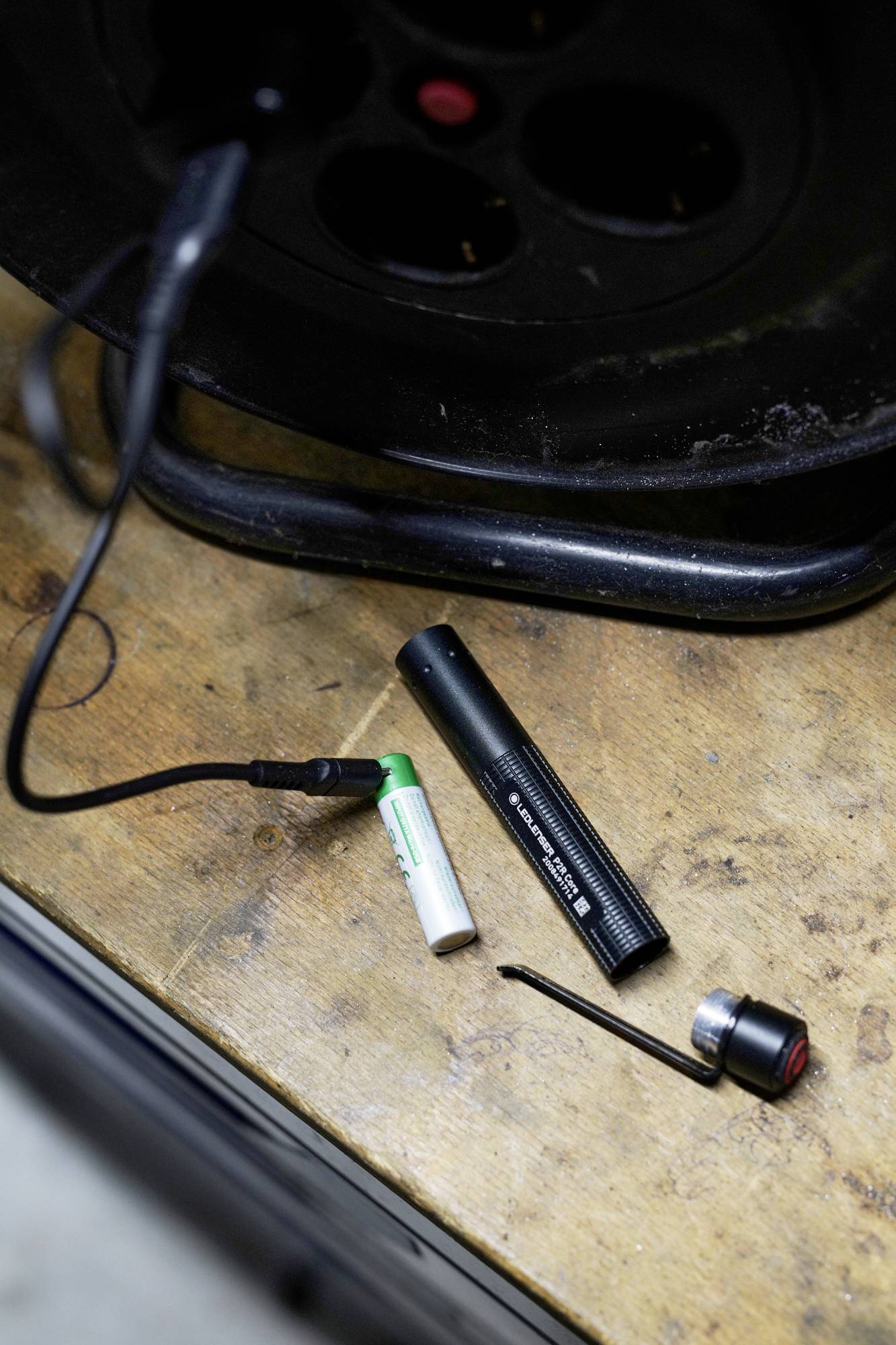 Batterier og oplader på et træbord. En sort cylinder og et delvist opladet batteri er synlige.