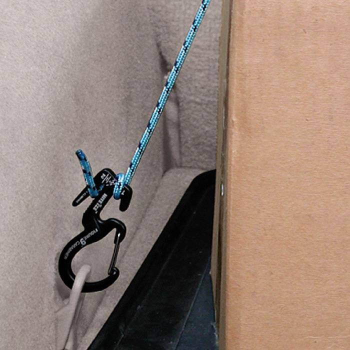 Blå snor ført gennem en sort plastikclips, fastgjort til en pap; bruges til sikring eller fastgørelse.