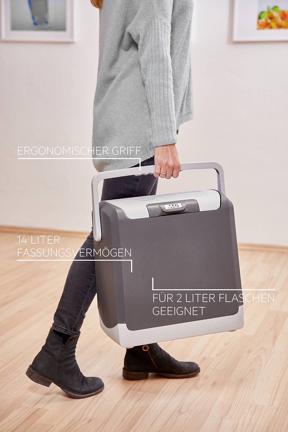 En person bærer et bærbart køleskab med ergonomisk håndtag. Påskrifter viser '14 liters kapacitet' og 'Egnet til 2-liters flasker'.