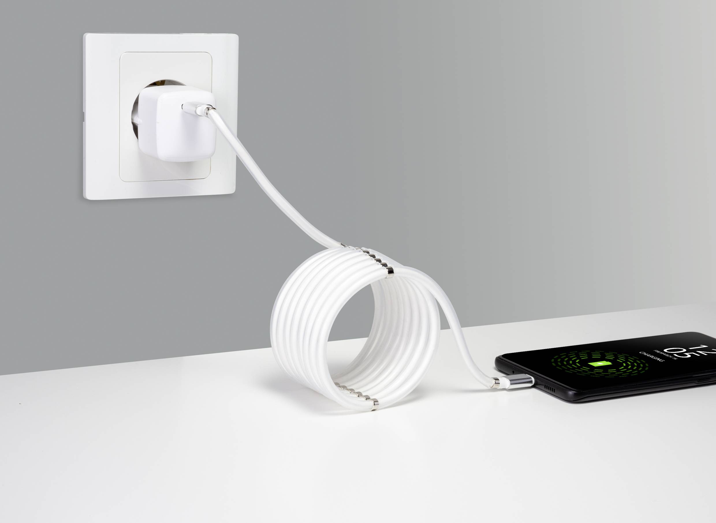 En smartphone oplades med en lang hvid USB-kabel ved en oplader i en stikkontakt og viser en opladningsskærm.