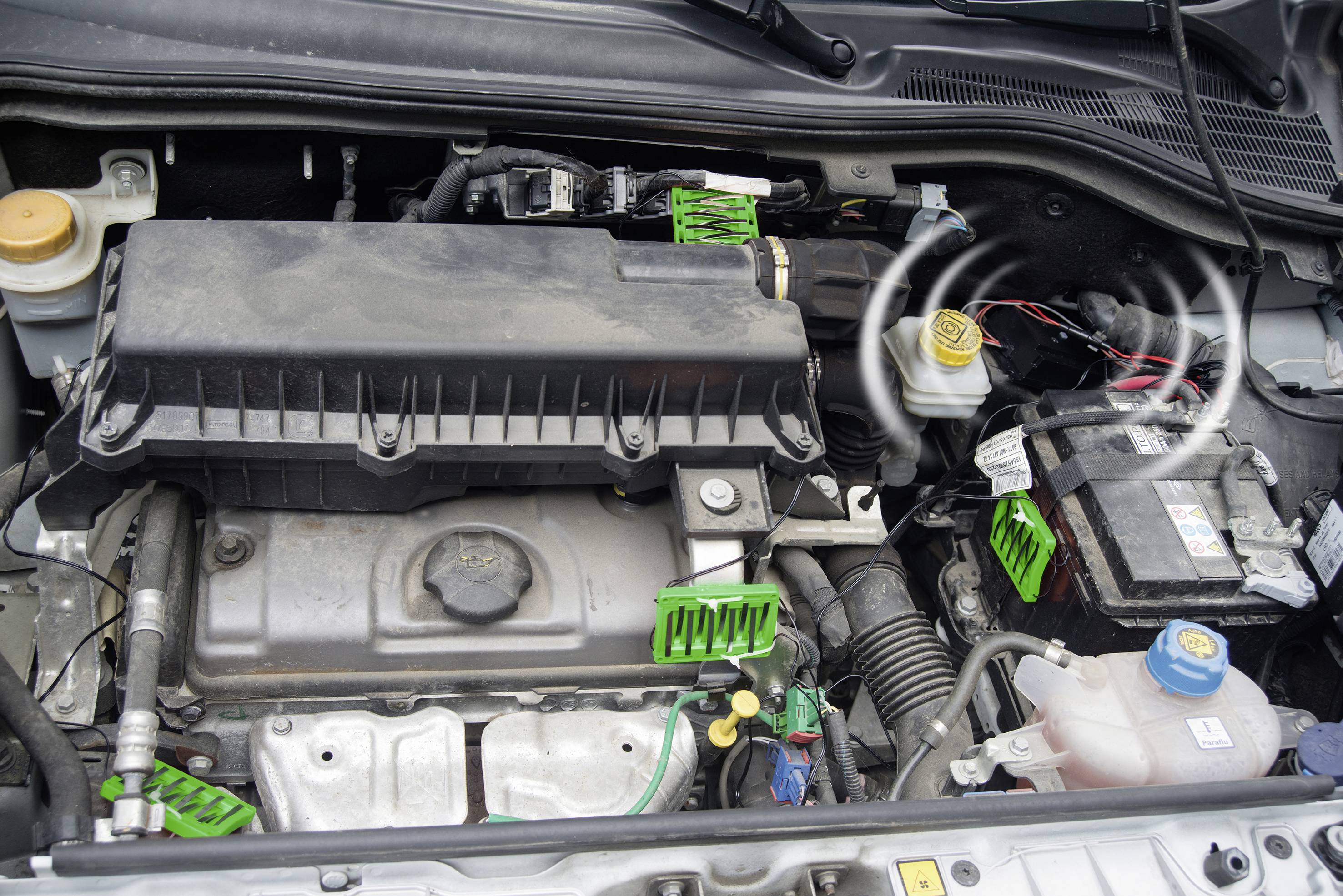 En åben bilmotor med synlige komponenter, herunder batteri, luftfilterhus, kølervæskebeholder og slanger.