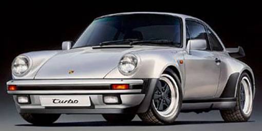 En sølvfarvet bil, Porsche 911 Turbo, med brede skærme og karakteristisk baghjulsspoiler, holder foran en mørk baggrund.
