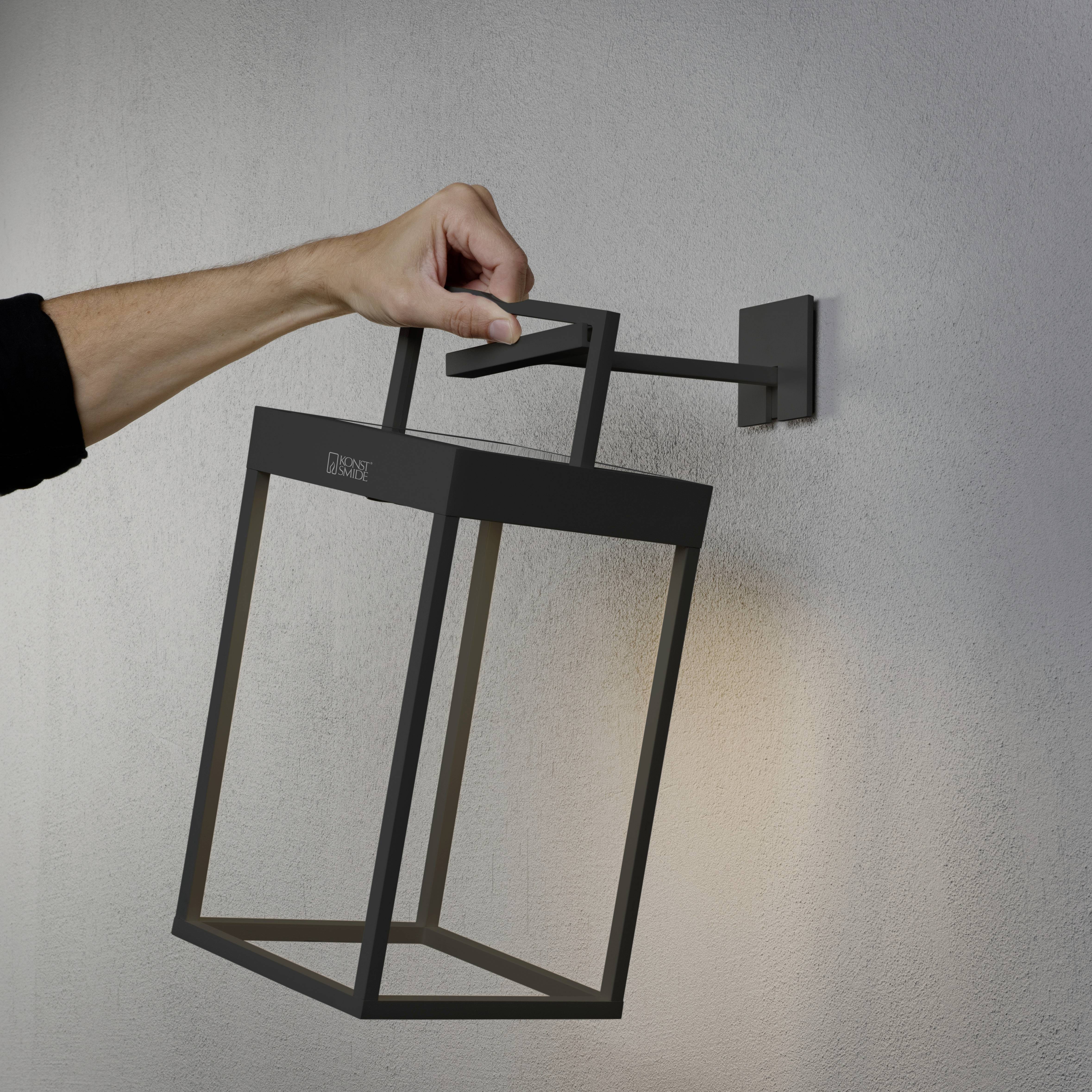 En hånd holder en moderne, rektangulær udendørs væglampe på en væg, der er indrettet i en minimalistisk stil.