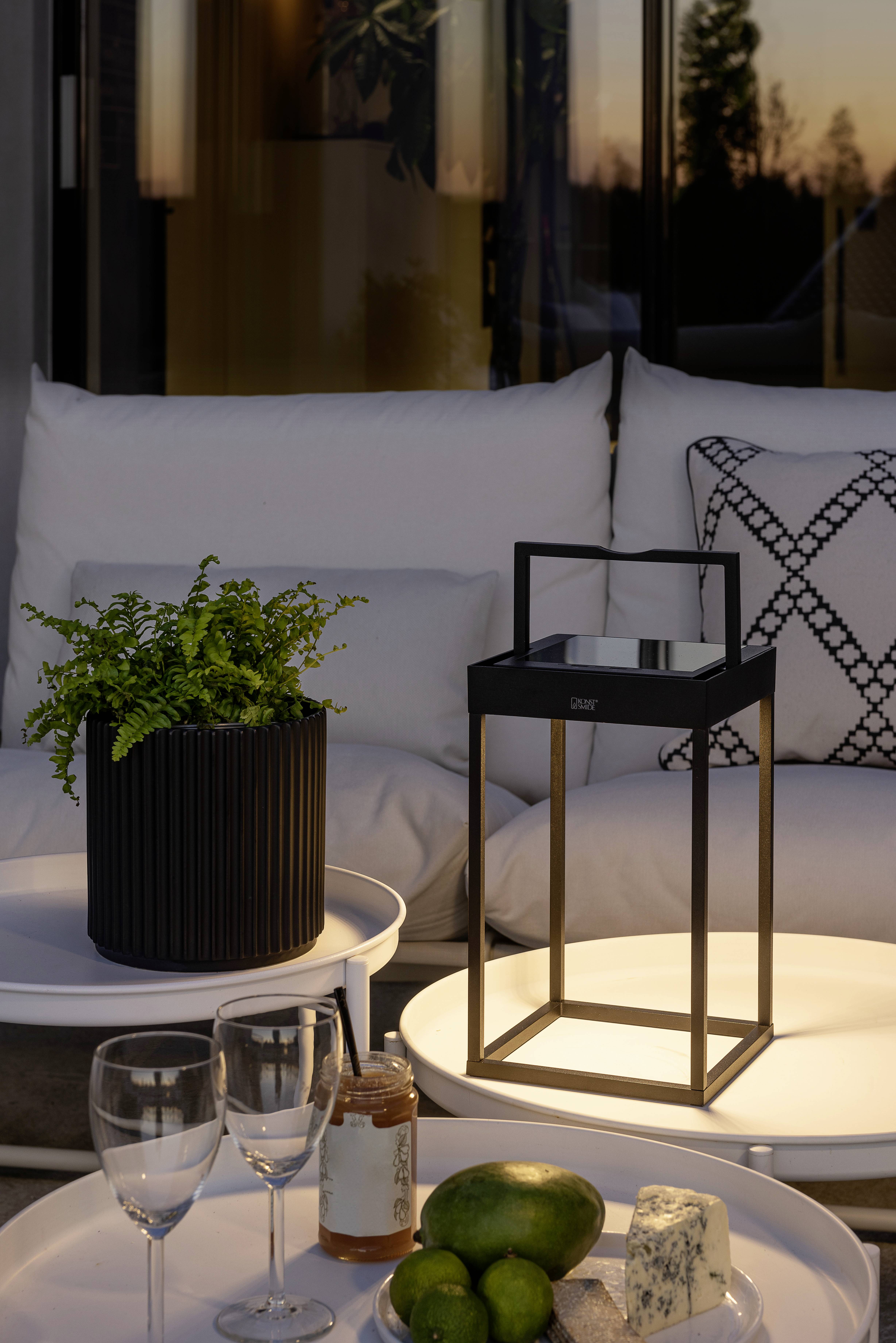 En terrasse ved solnedgang med en hyggelig siddegruppering, hvor et bord er pyntet med planter, en lampe og fade med frugt og ost.