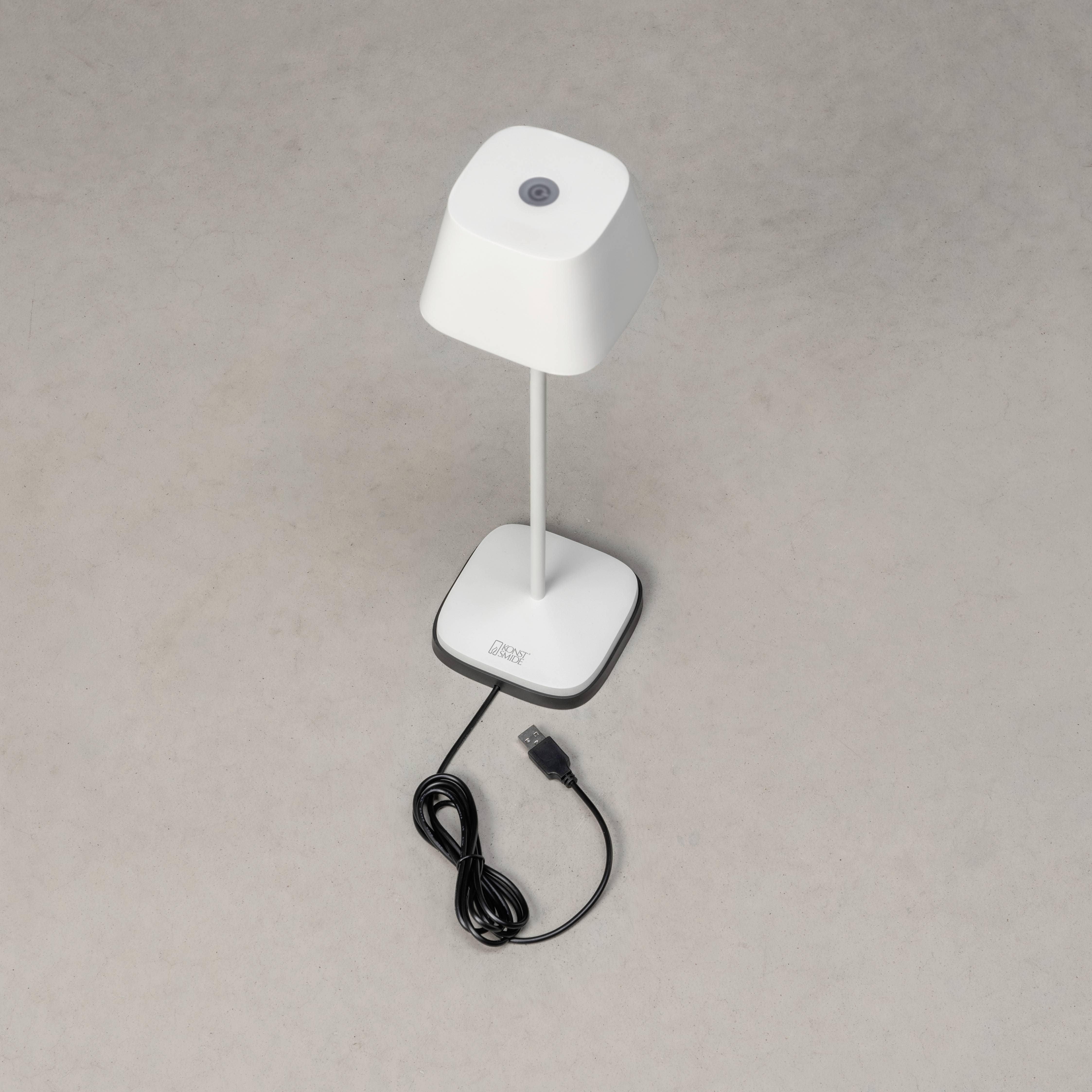 Hvid bordlampe med firkantet lampeskærm og USB-kabel på grå baggrund.