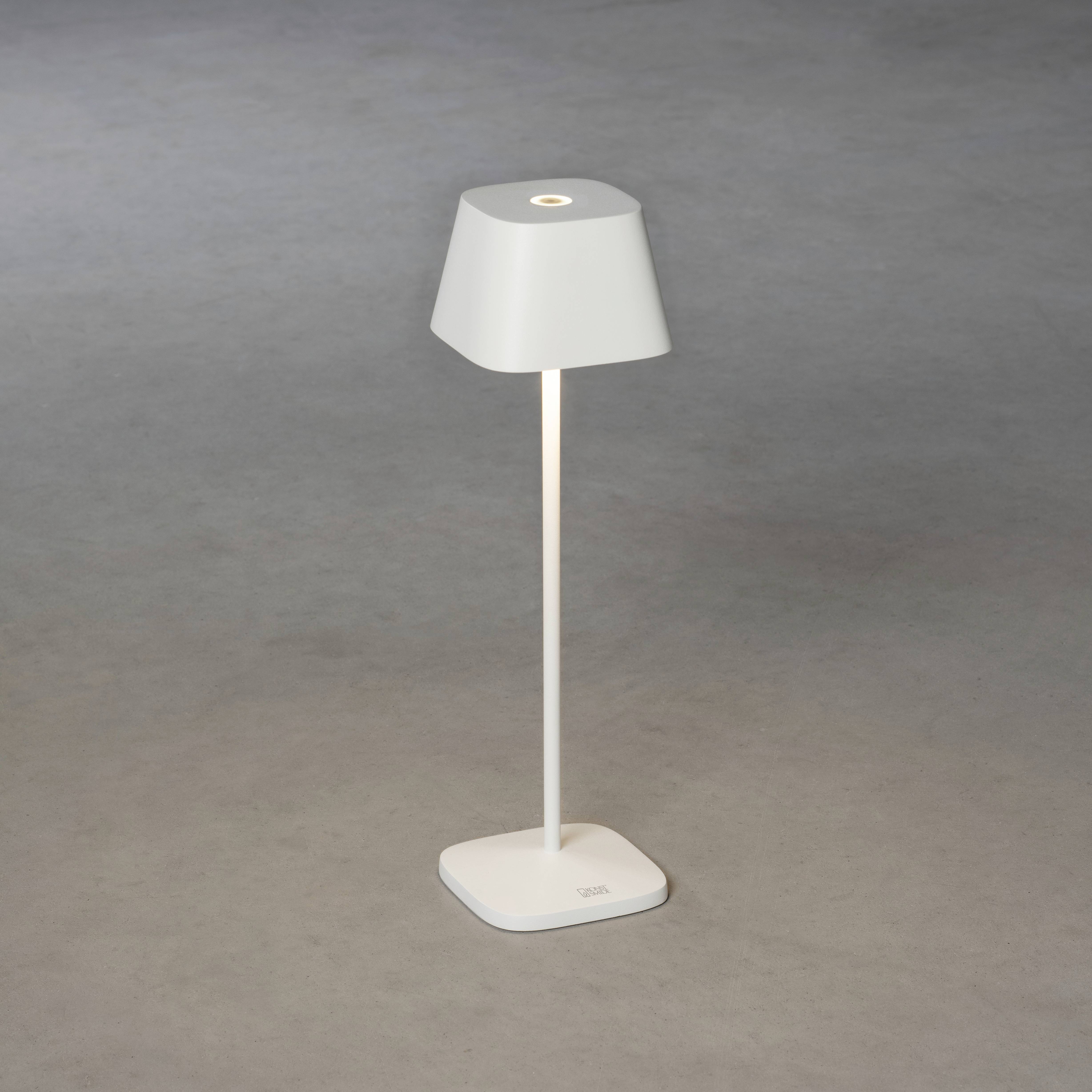 Et moderne, grå bordlampe på en enkel, firkantet base, stående på et gråt gulv.