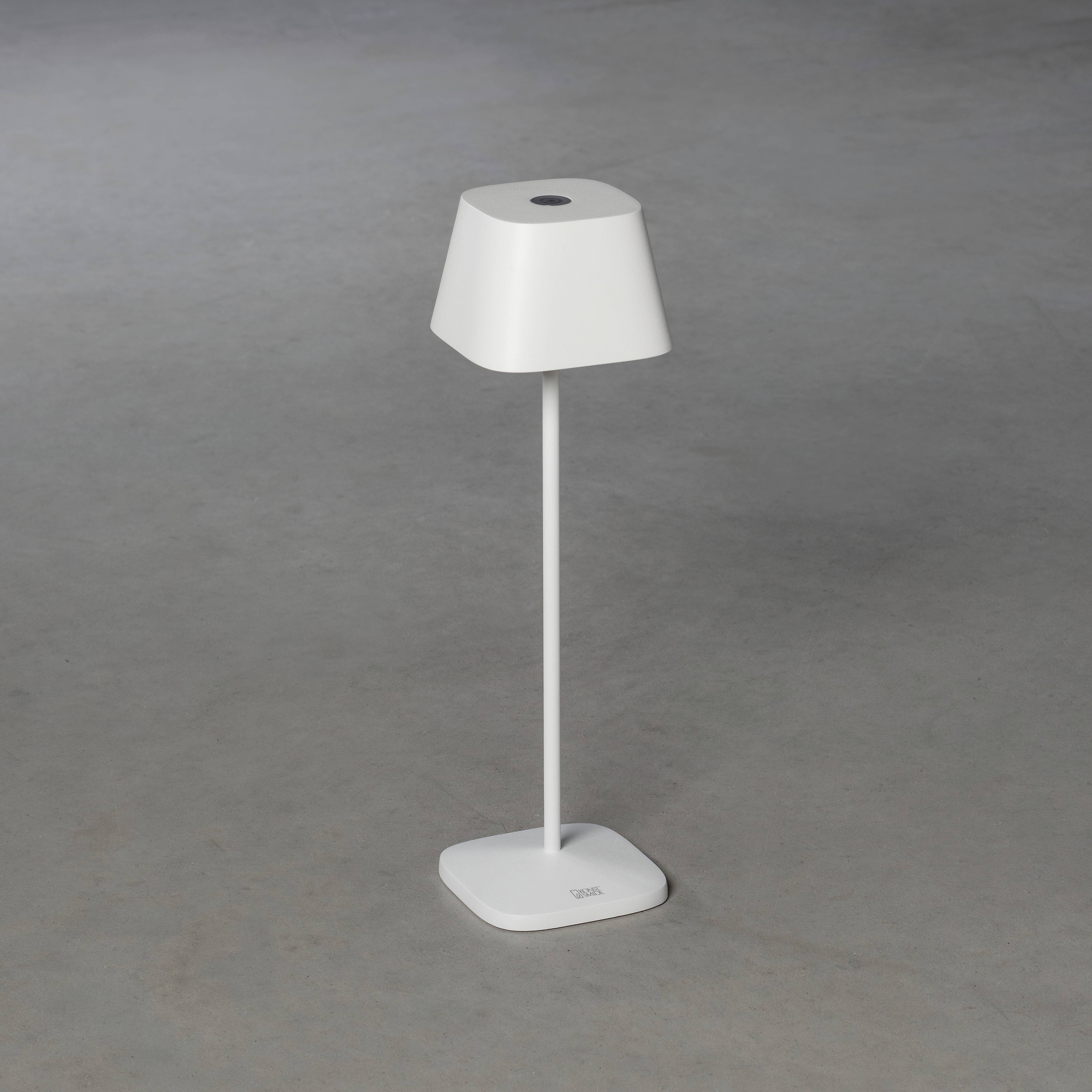 Lille, hvid bordlampe med firkantet base og skråt lampeskærm, stående på grå gulv.
